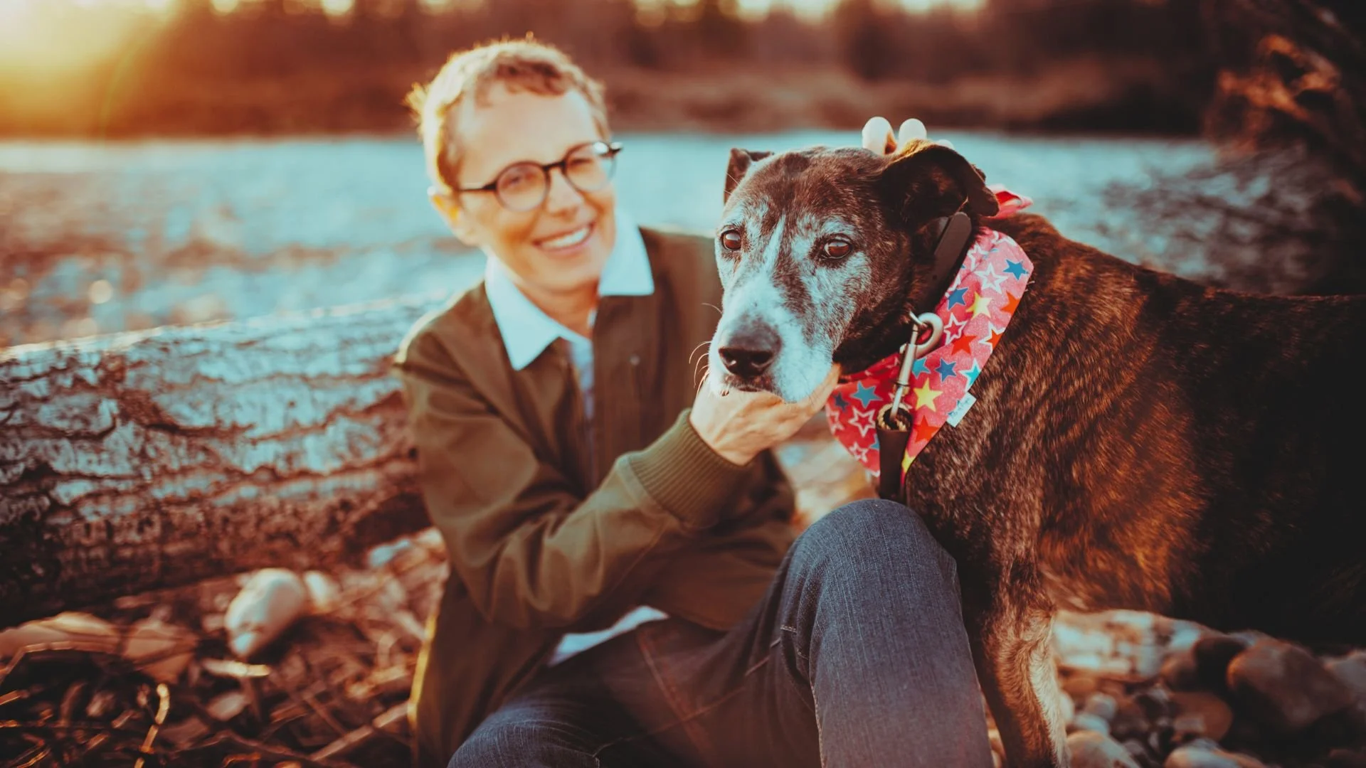 A woman with glasses sits on a log with a dog, representing Therapy Tails Level 2 ImPAWSible Possible in Calgary.