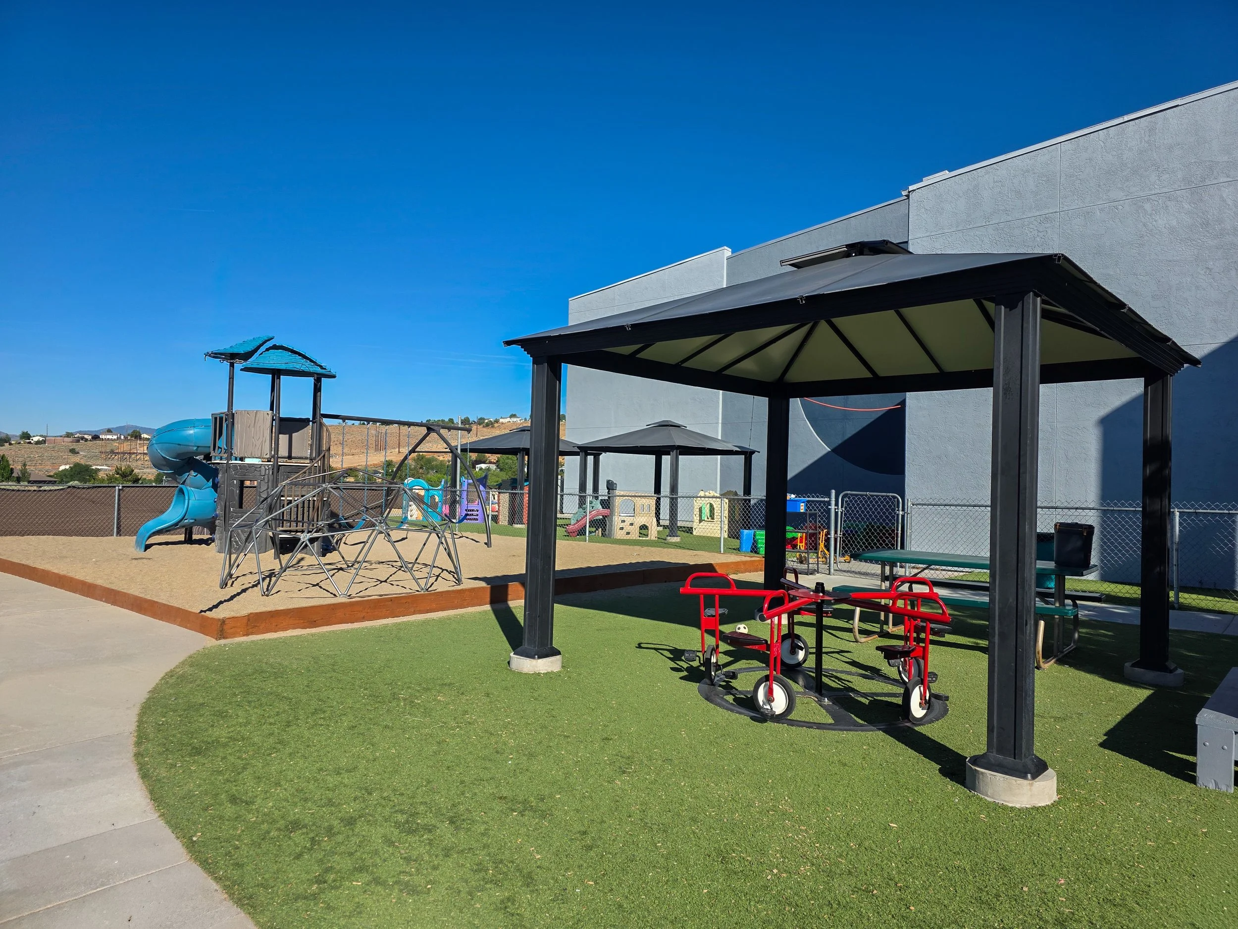 Outdoor learning and play area at Little Lites Christian Learning Center in Reno, Nevada. Featuring shaded gathering spaces, ride-on toys, climbing equipment, and open areas for play, our Christian preschool and childcare program provides children wi