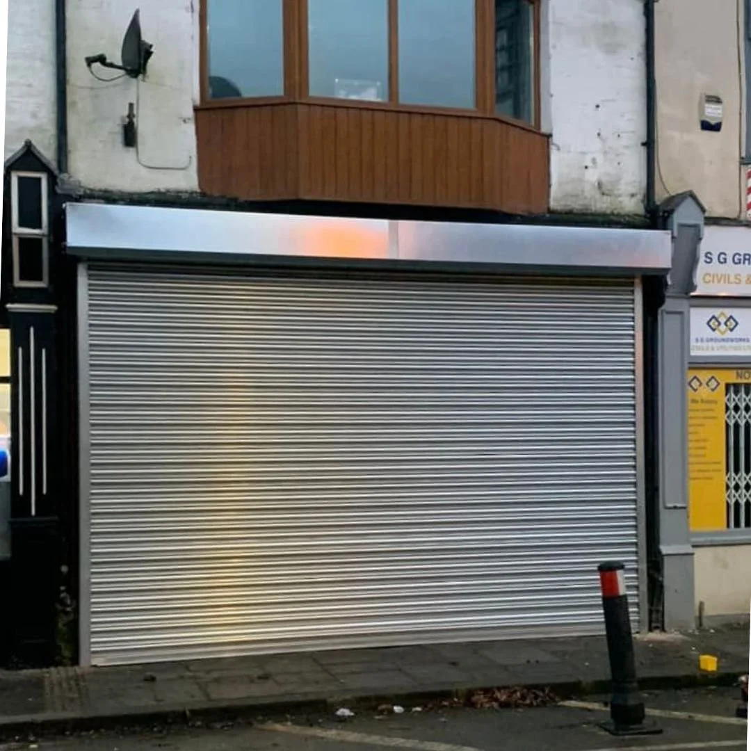 Shop front protected by a sleek silver roller shutter, fully closed.