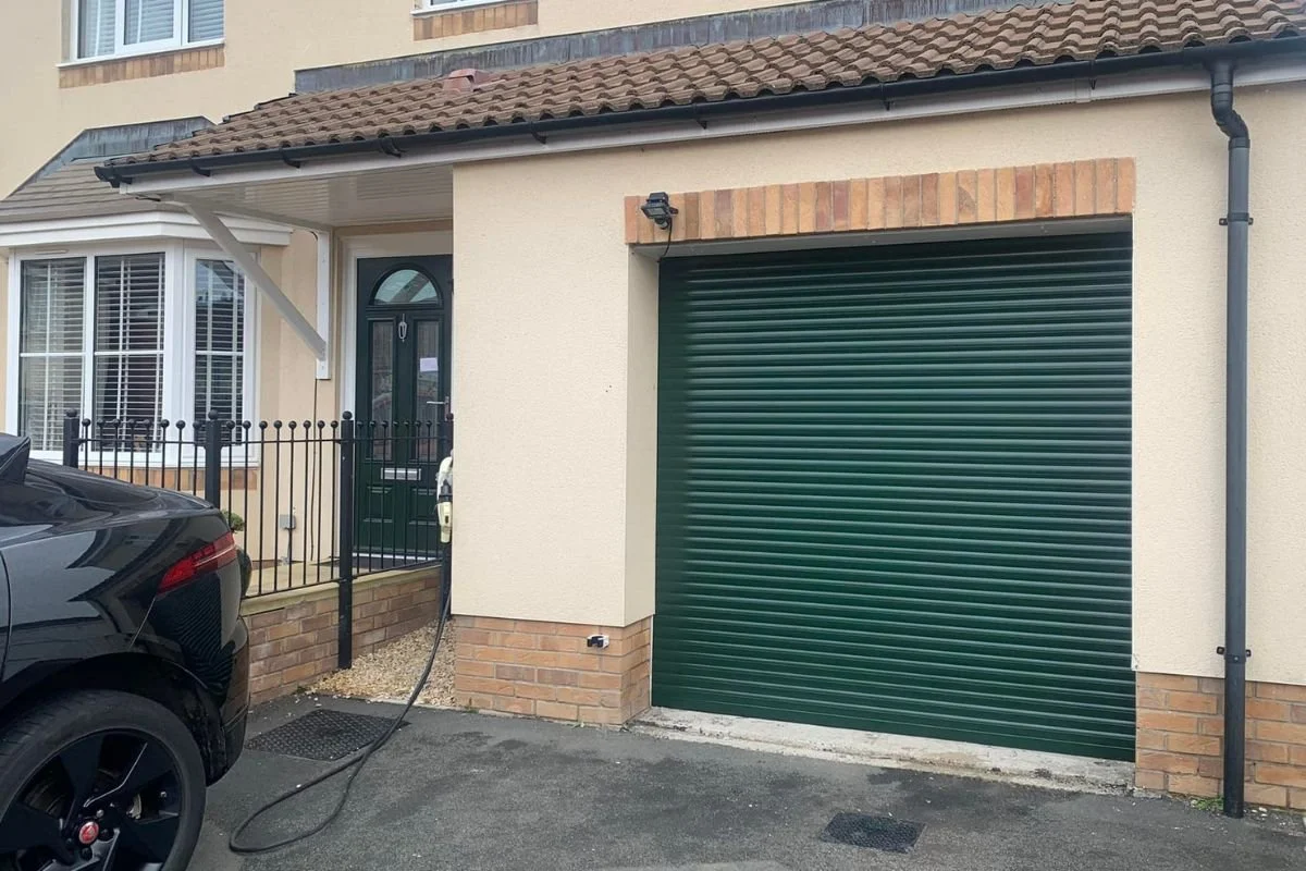 A residential roller shutter door next to a front home door, both in the same dark green colour.
