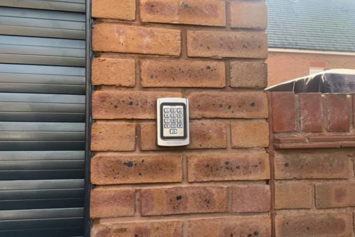 A silver pin pad next to the side of a black roller shutter door.