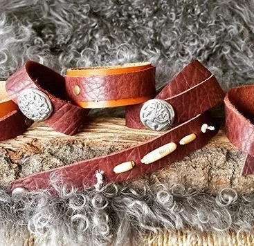Leather wristbands, some with decorative silver accents, arranged on a piece of wood surrounded by curly silver-gray hair or fur.