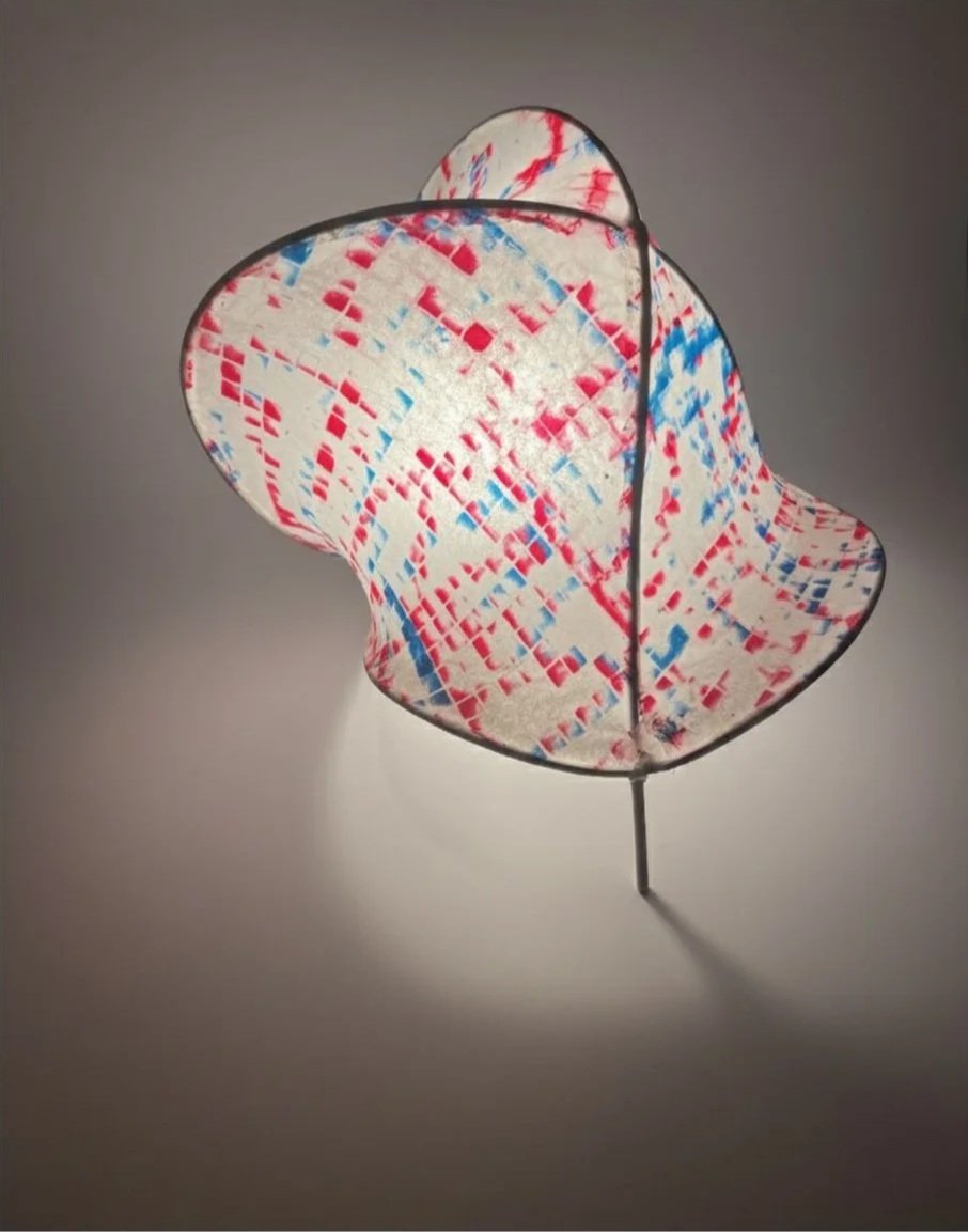 Colorful paper lantern with red and blue geometric patterns and a black wire frame, casting a shadow on the wall.