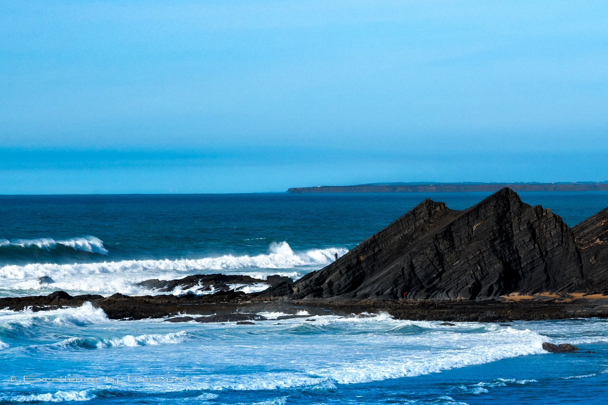 Rocky coastal landscape with ocean waves and blue sky.