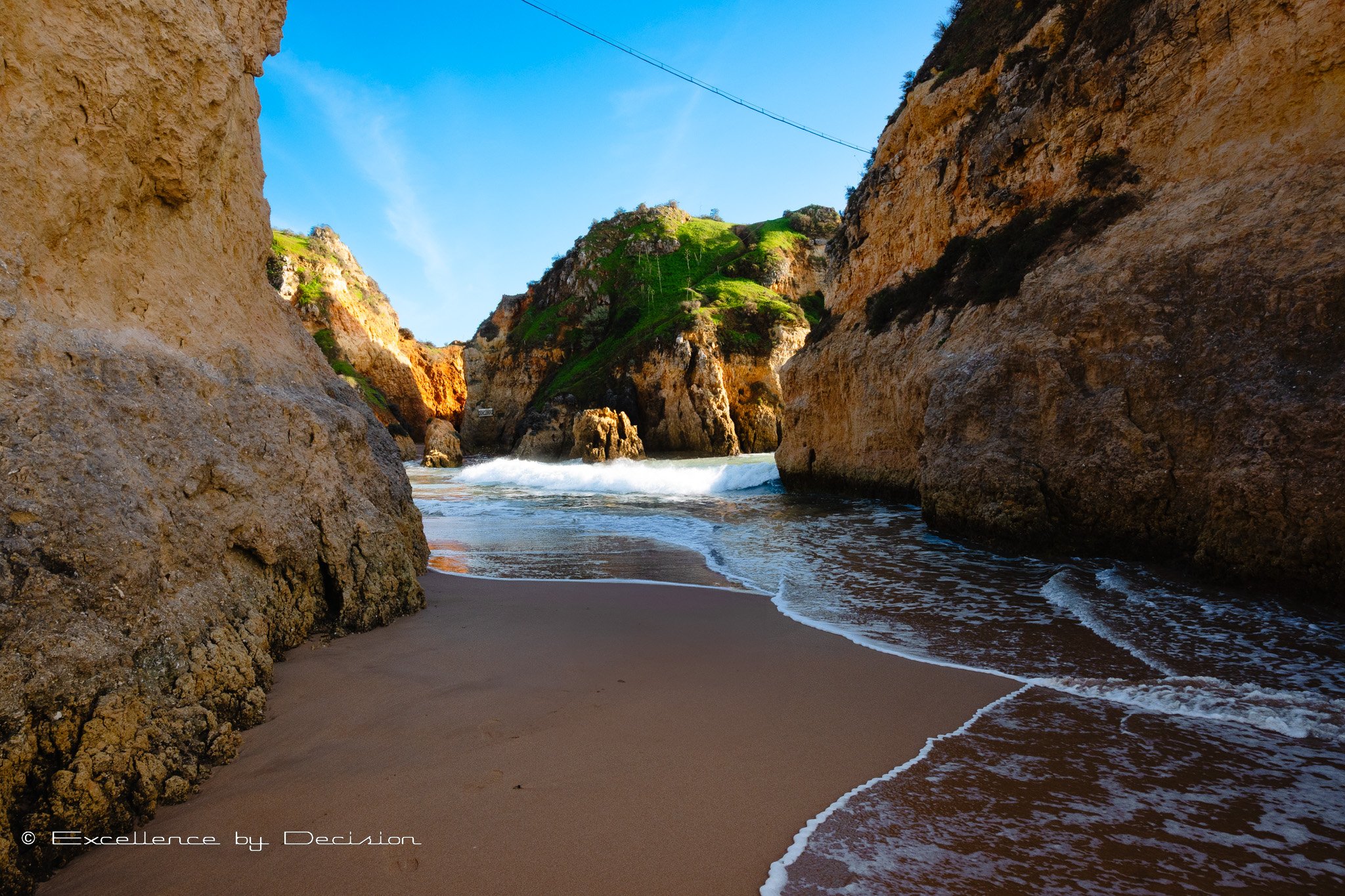 Rocky coastal landscape with sandy beach and ocean waves under blue sky