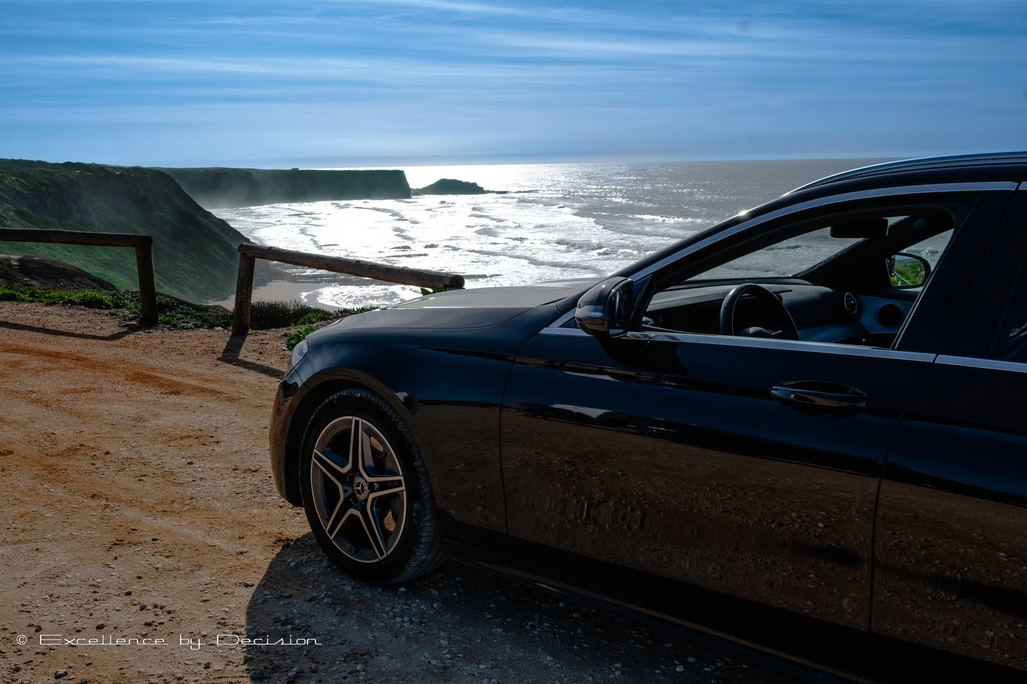 Black car parked on a coastal cliff with ocean view
