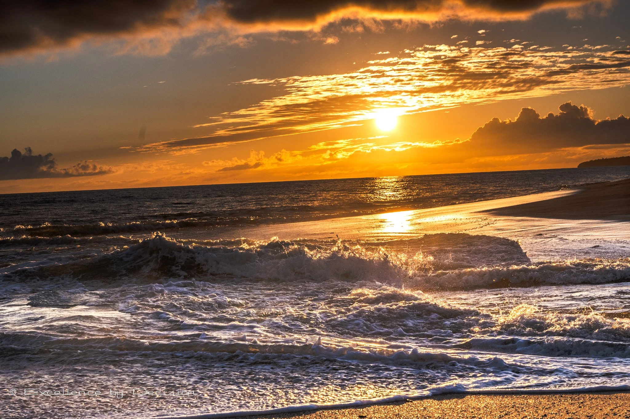 Sunset over ocean waves with golden sky and clouds.