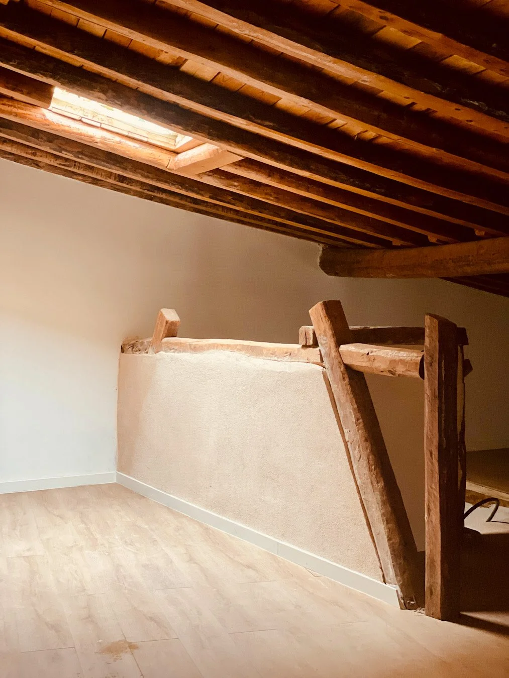 Imagen de un ático con techo de madera, una pared blanca y una escalera de madera.