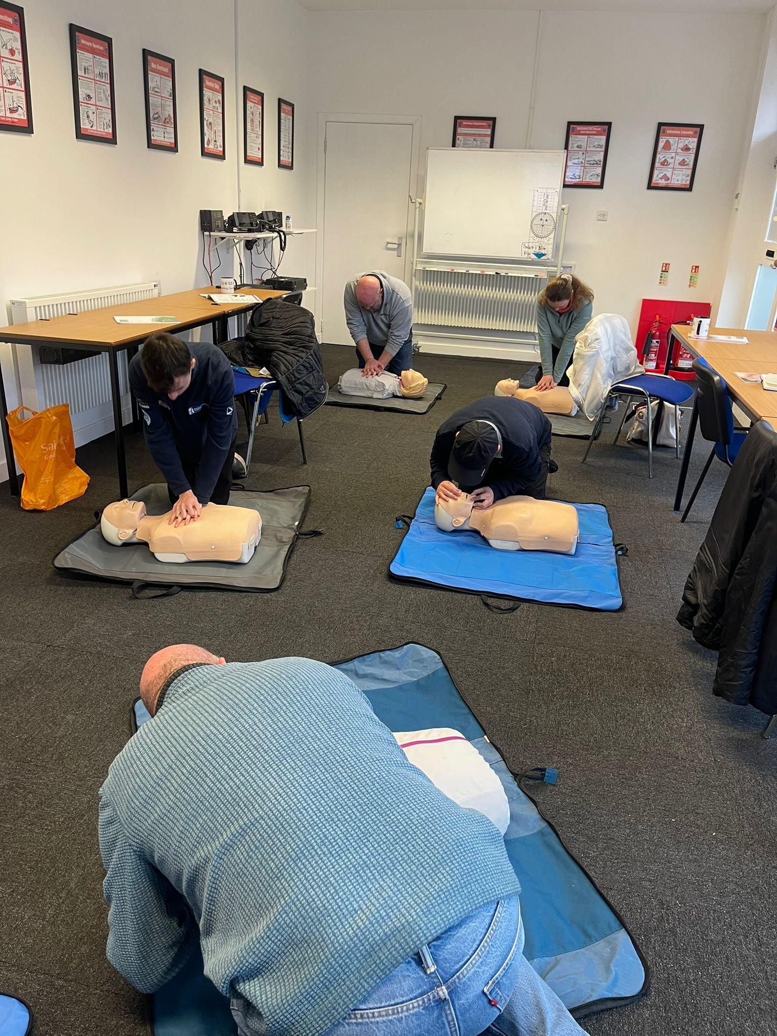 People participating in a CPR training class, practicing on mannequins in a classroom.