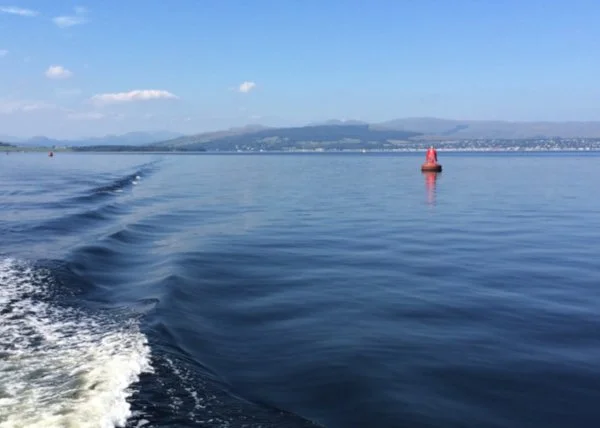 an expanse of sea with a single red marker buoy and a stern wash from a boat