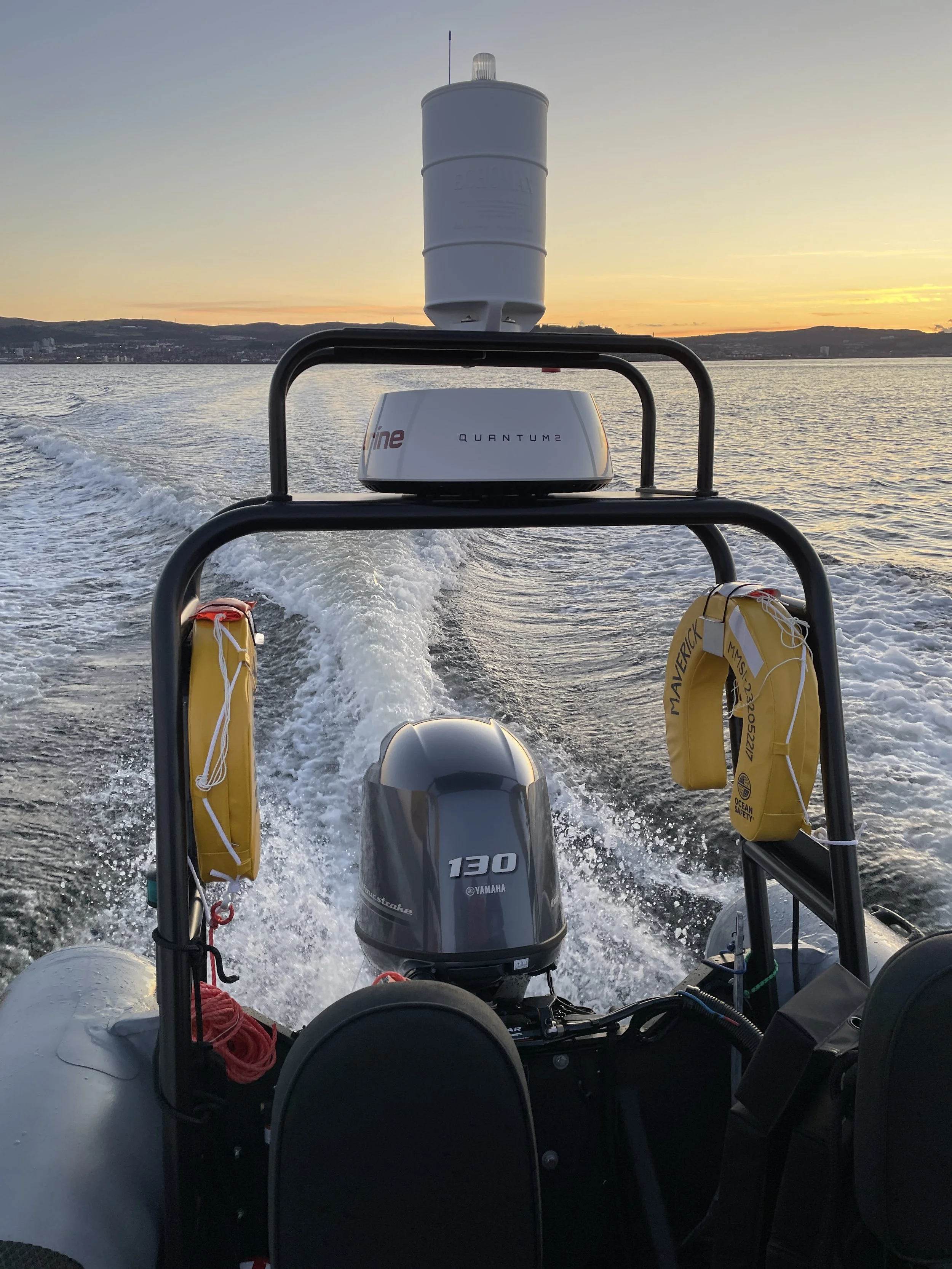 View from the back of a boat at sunset, showing the Yamaha 130 outboard motor, a ship’s radar and GPS equipment, life jackets, and the wake behind the boat as it moves across the water.