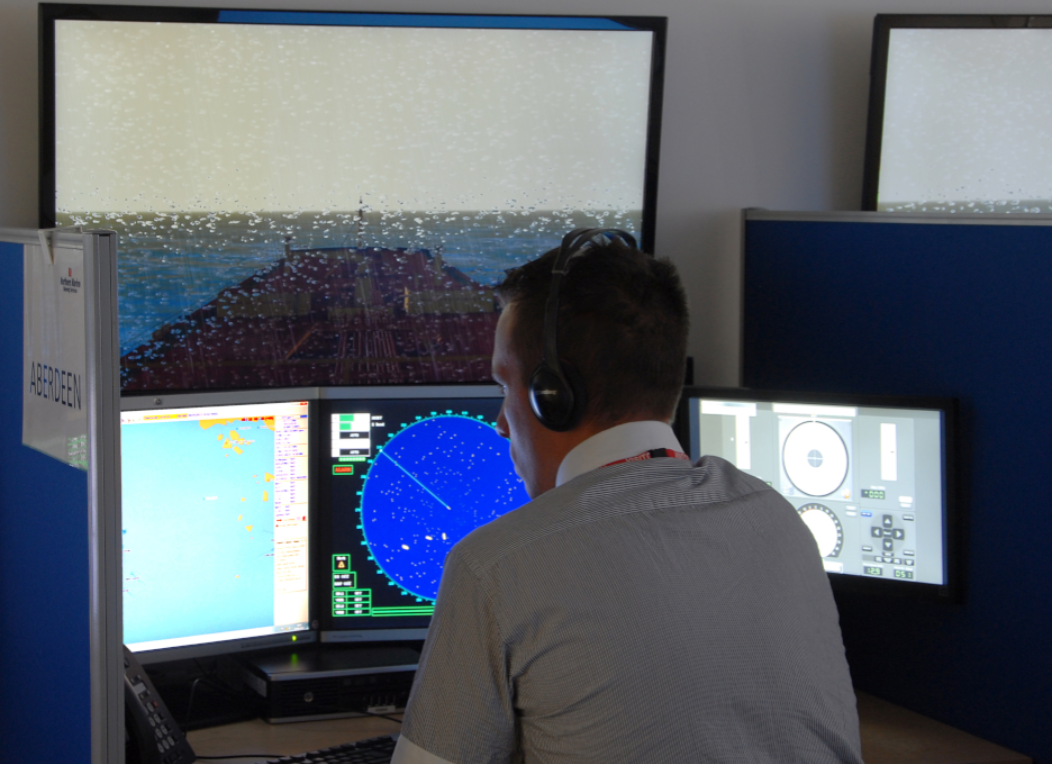 A man wearing a headset working at a radar and navigation station with multiple monitors displaying ocean maps and radar data.