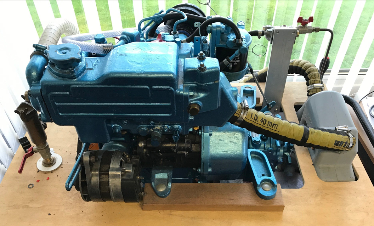 A blue diesel engine, used for training students, on a wooden table with various pipes and fittings.