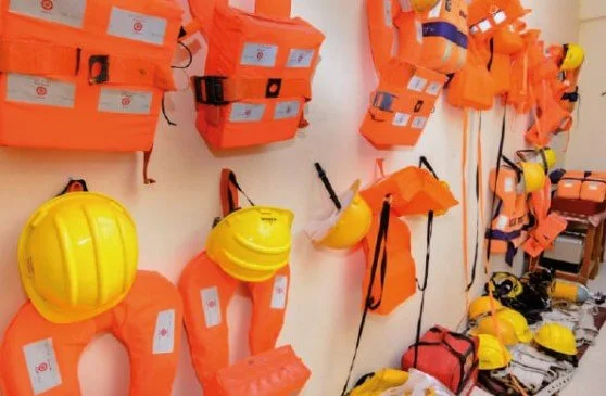 Safety equipment including life jackets, helmets, and buoyancy devices displayed on a wall.