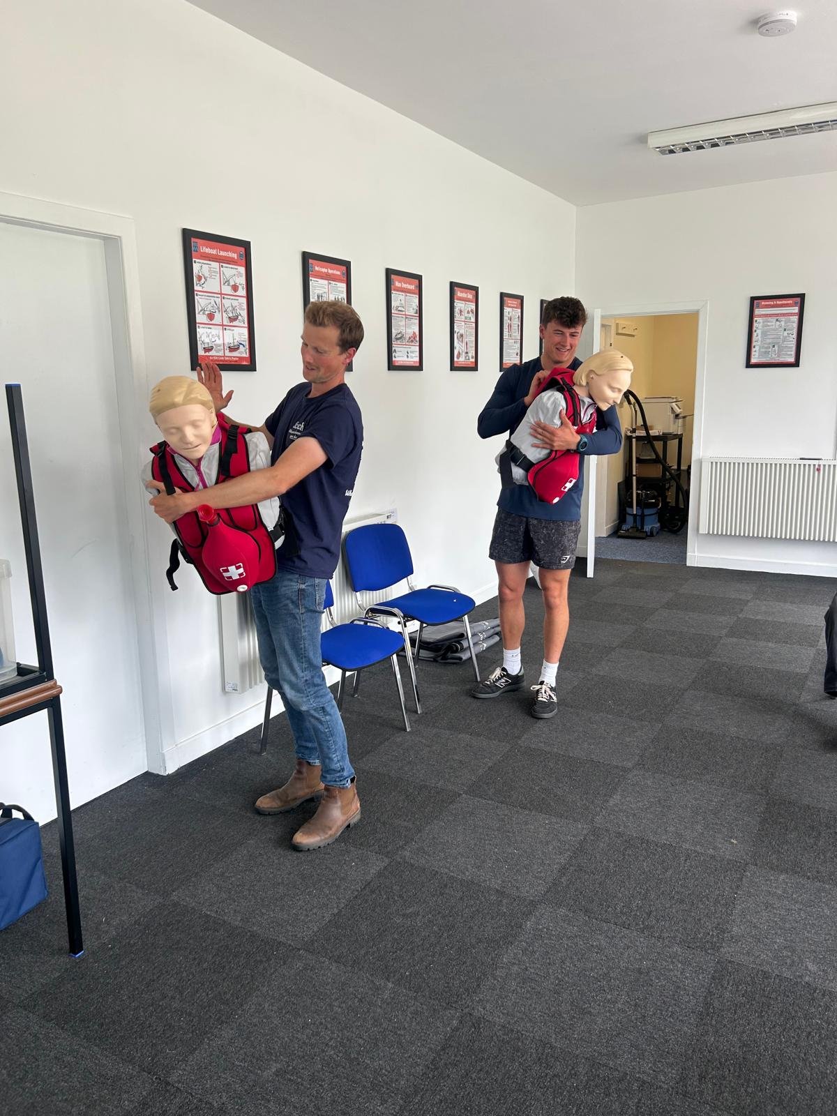 Two people practicing emergency first aid techniques using training mannequins in a classroom