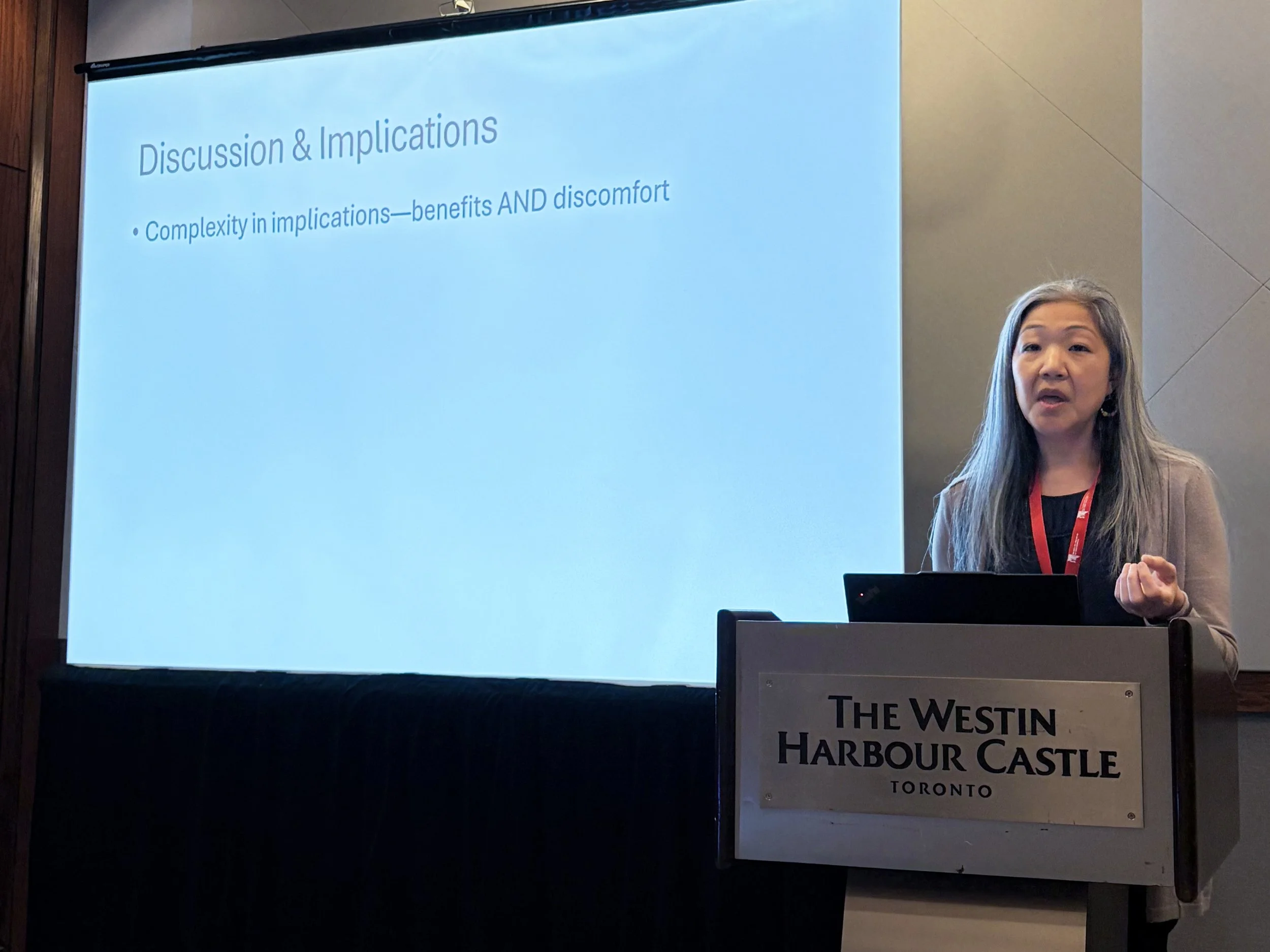 Lisa Kiang gives a presentation standing at a dais, next to a projector screen.