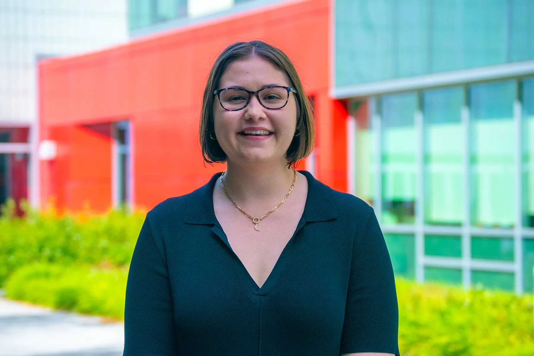 Woman stands in front o fa building with a red and glass facade