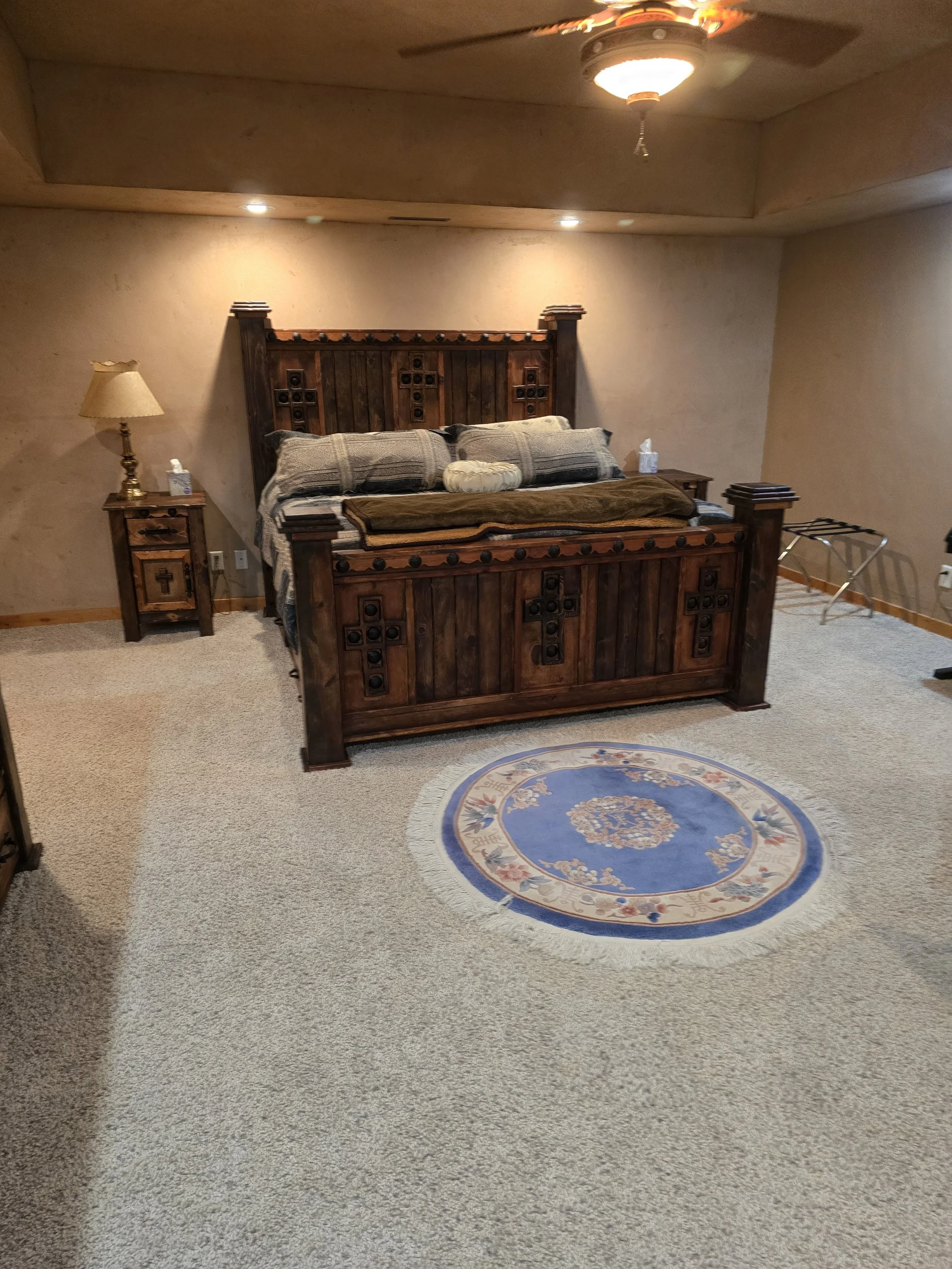 Bedroom with wooden bed frame, nightstand, and lamp, carpet floor, circular rug, and ceiling fan.
