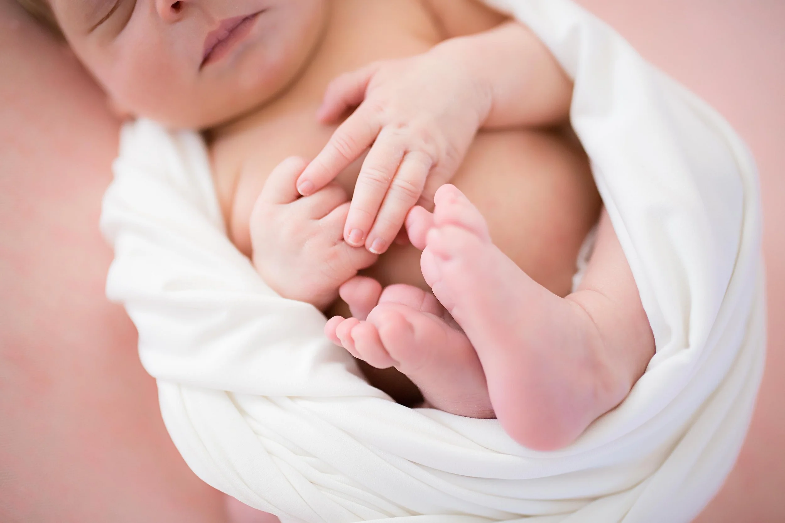 Close-up of a newborn baby and an adult, likely the mother, holding their hands together.