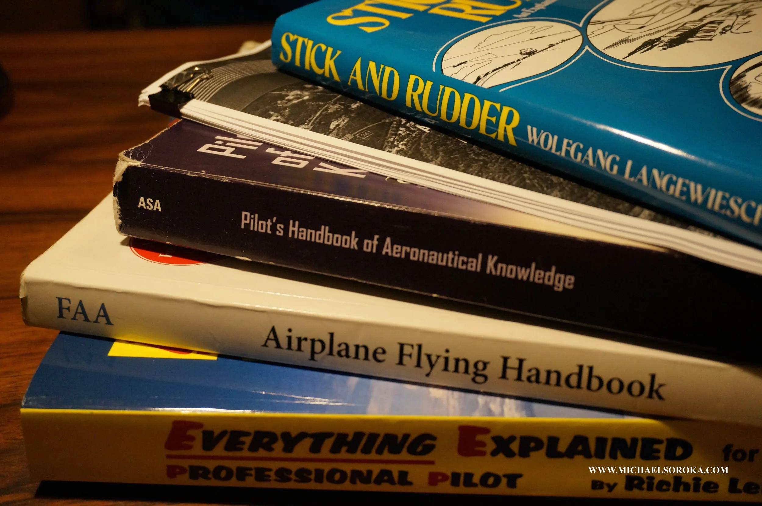 Stack of aviation books including "Stick and Rudder," "Pilot's Handbook of Aeronautical Knowledge," "Airplane Flying Handbook," and "Everything Explained for the Professional Pilot."