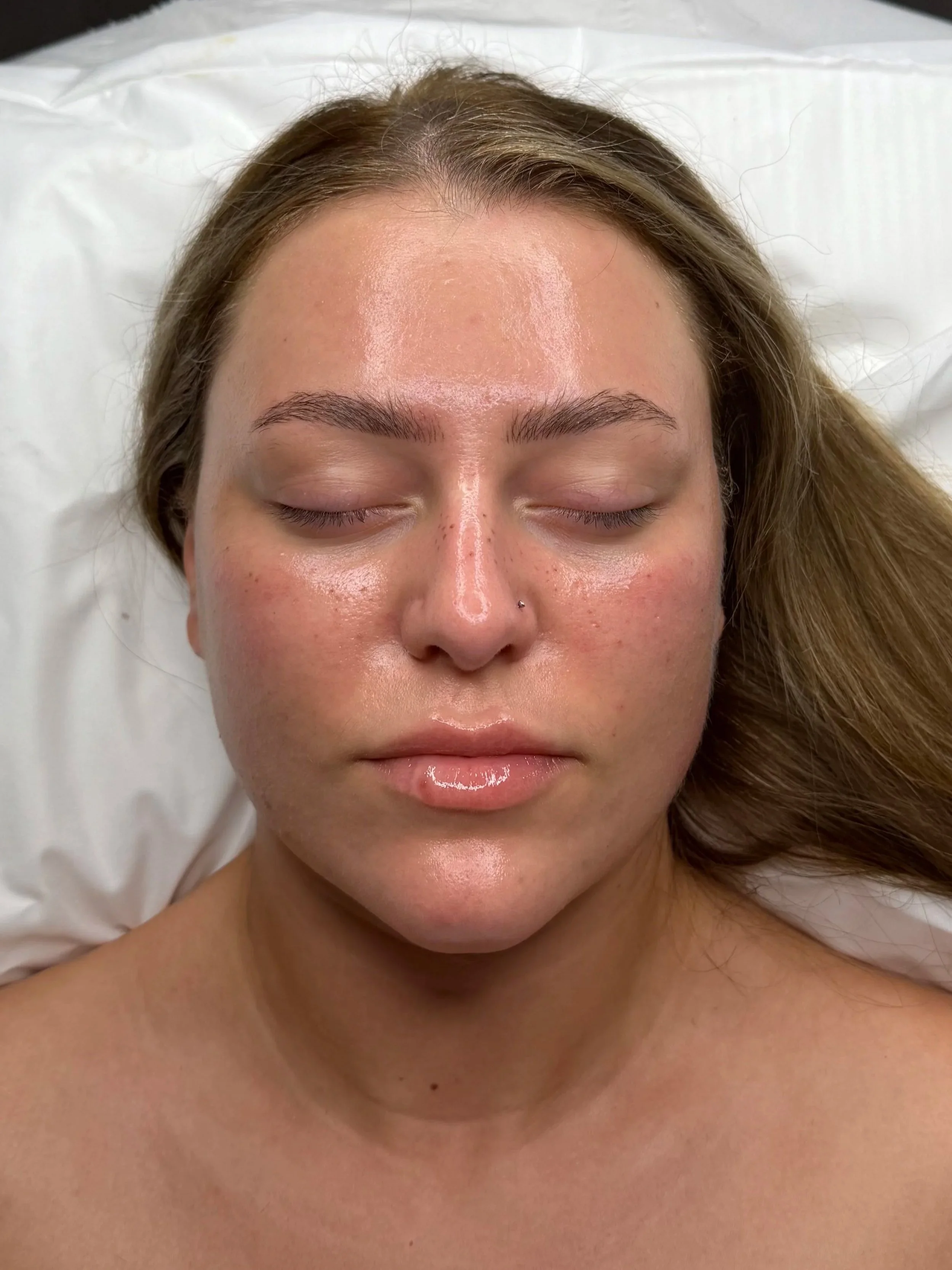 Close-up of a woman with light skin, closed eyes, and wet skin, lying on a white pillow.