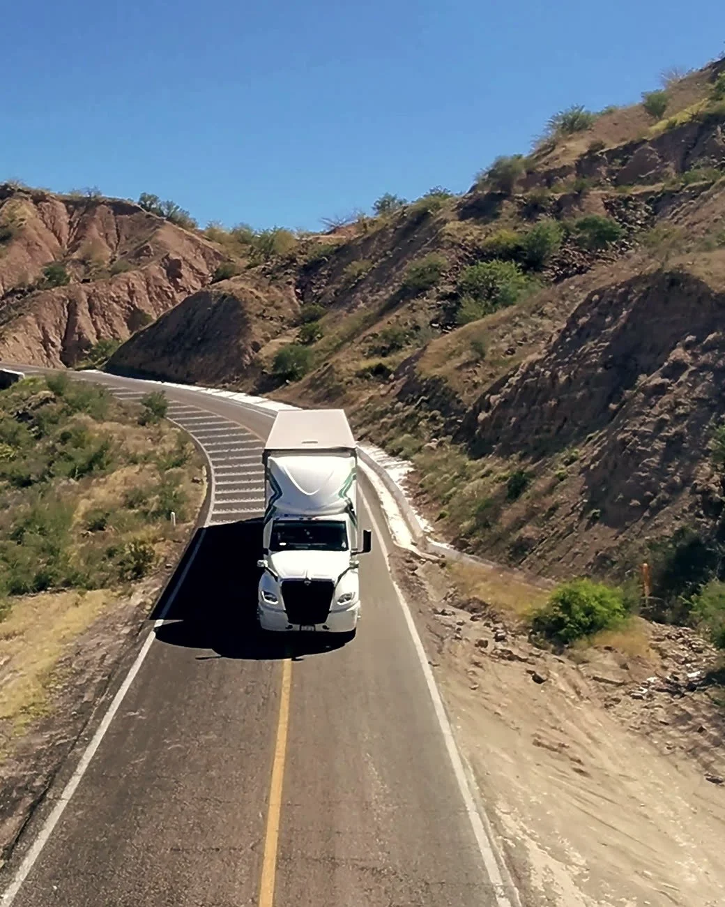 White semi truck on a two-lane highway through the hills