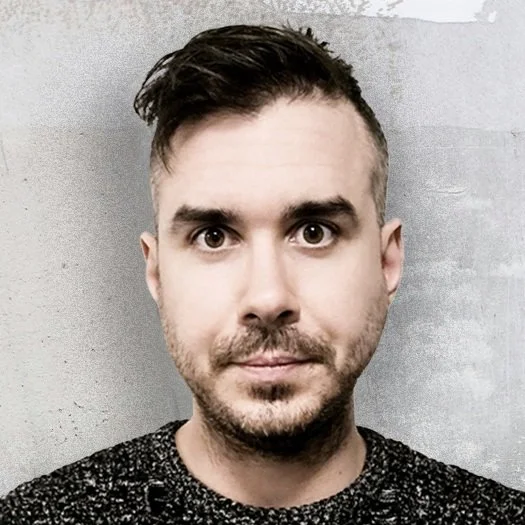 Man with short hair standing against a gray textured background.