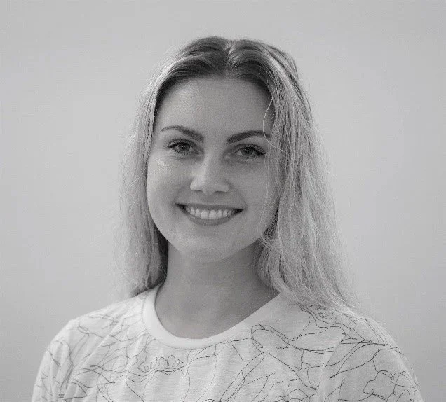 Black and white photo of a smiling woman with long hair, wearing a patterned shirt.