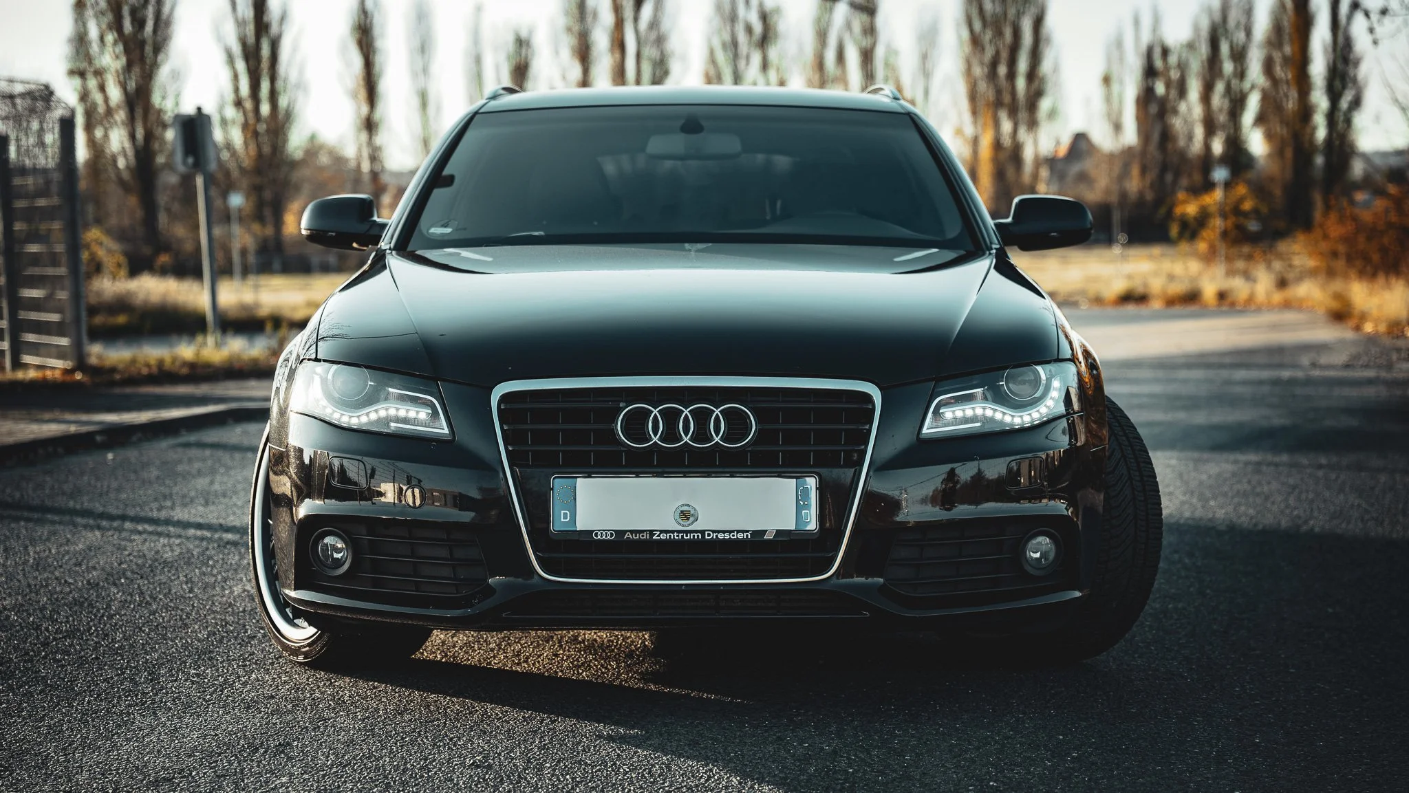 Black Audi sedan parked on a street with trees in the background, front view.