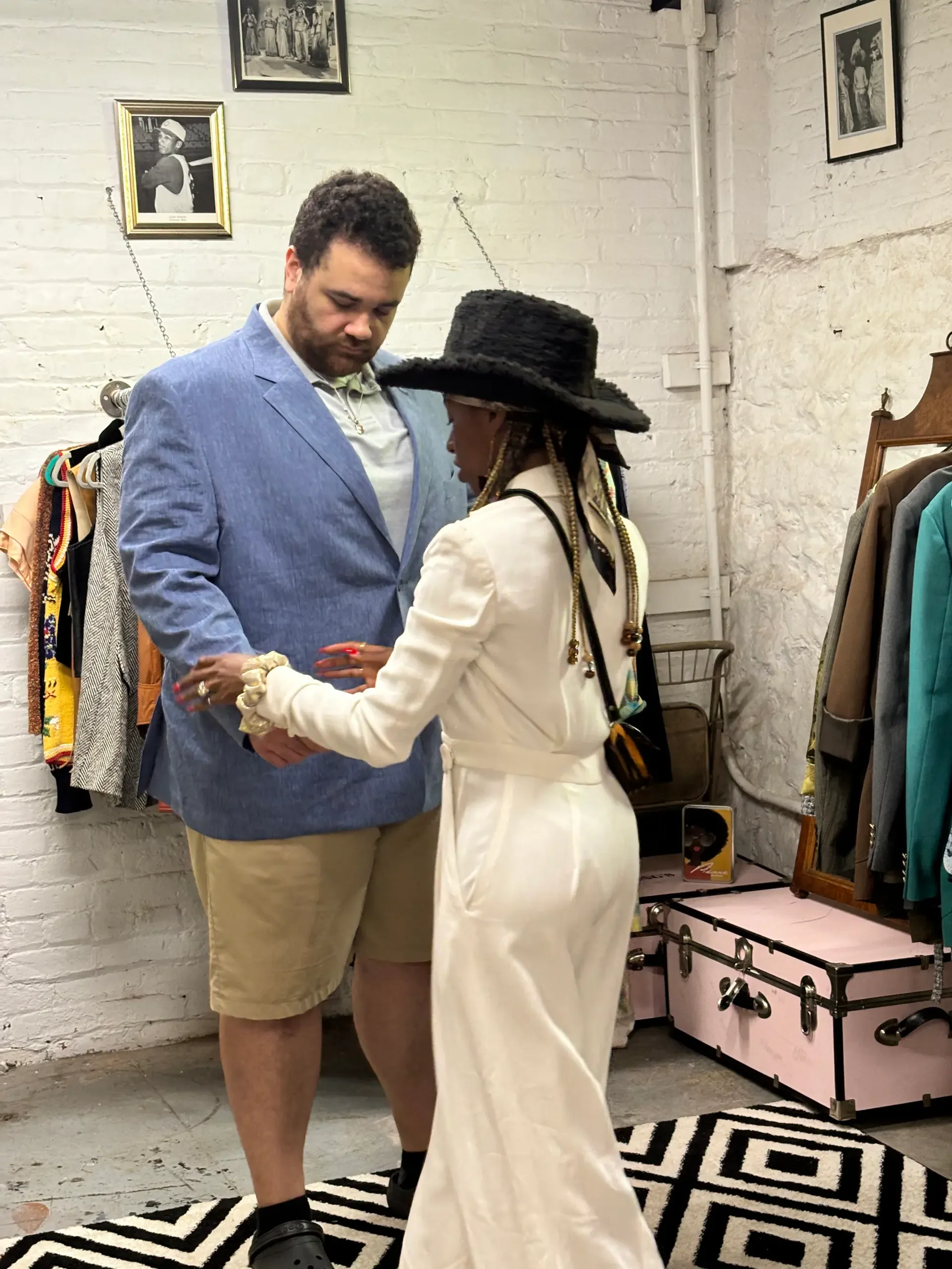 Personal styling session inside a vintage studio as a client tries on a blue blazer with guidance from a stylist, surrounded by curated garments and archival fashion pieces.