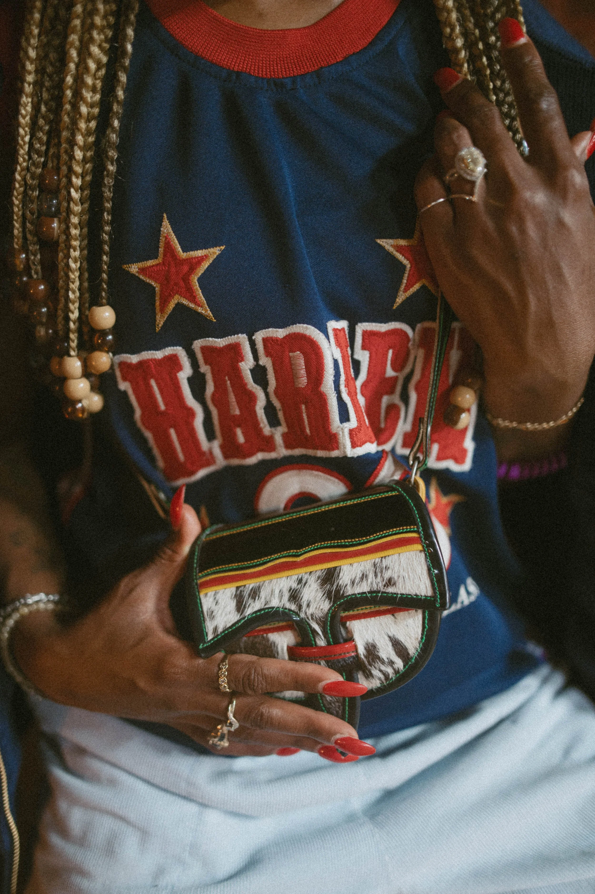 Close-up of a model wearing a vintage Harley-inspired jersey while holding a textured leather mini bag, styled with layered jewelry and braids, capturing the personal storytelling and individuality of archival fashion pieces.