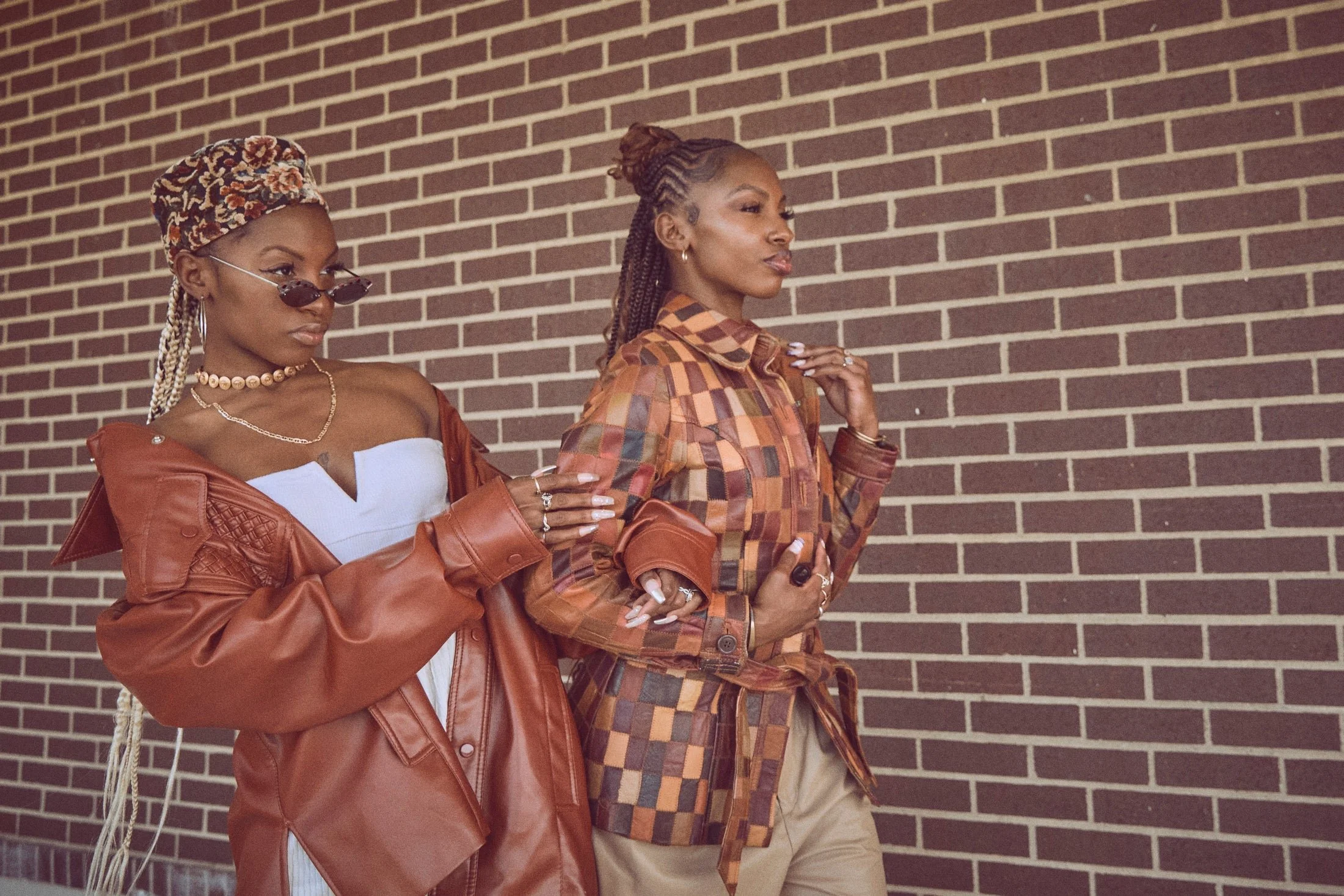 Two stylish women wearing vintage jackets in warm brown tones walking against a brick wall, showcasing statement outerwear pieces from Fashion to the People’s Premium Vintage collection.