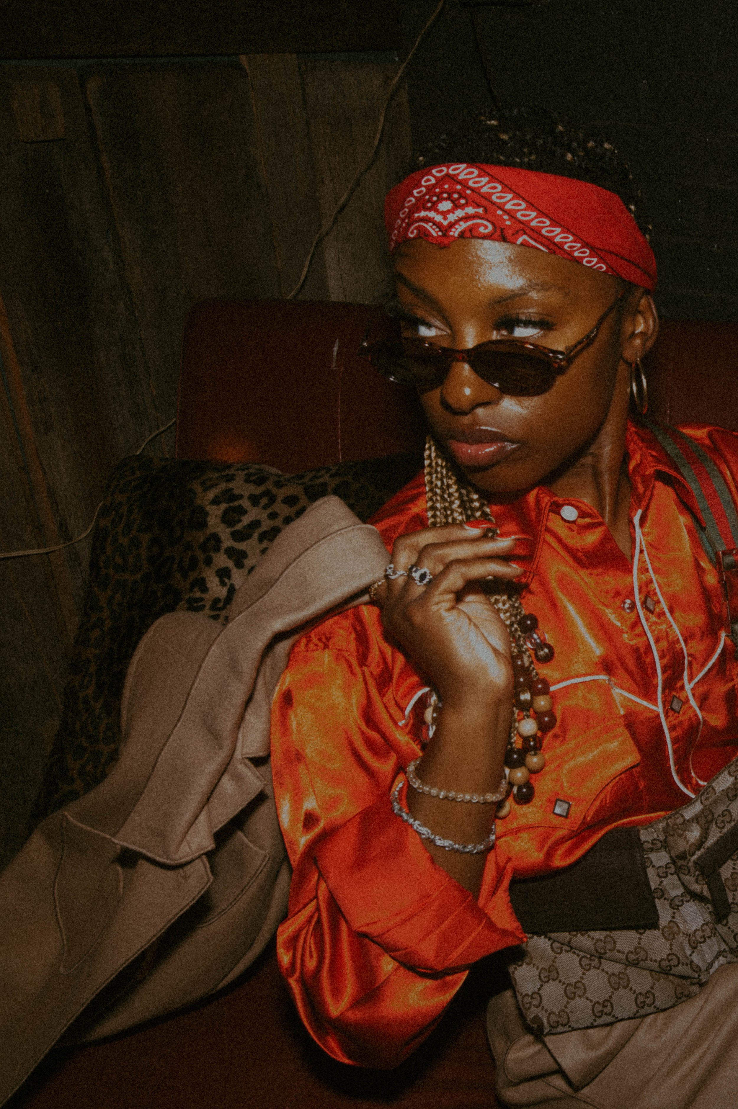 Kyetra wearing a red satin shirt and bandana with sunglasses, styled in an editorial vintage fashion setting with layered accessories and a relaxed, confident pose.