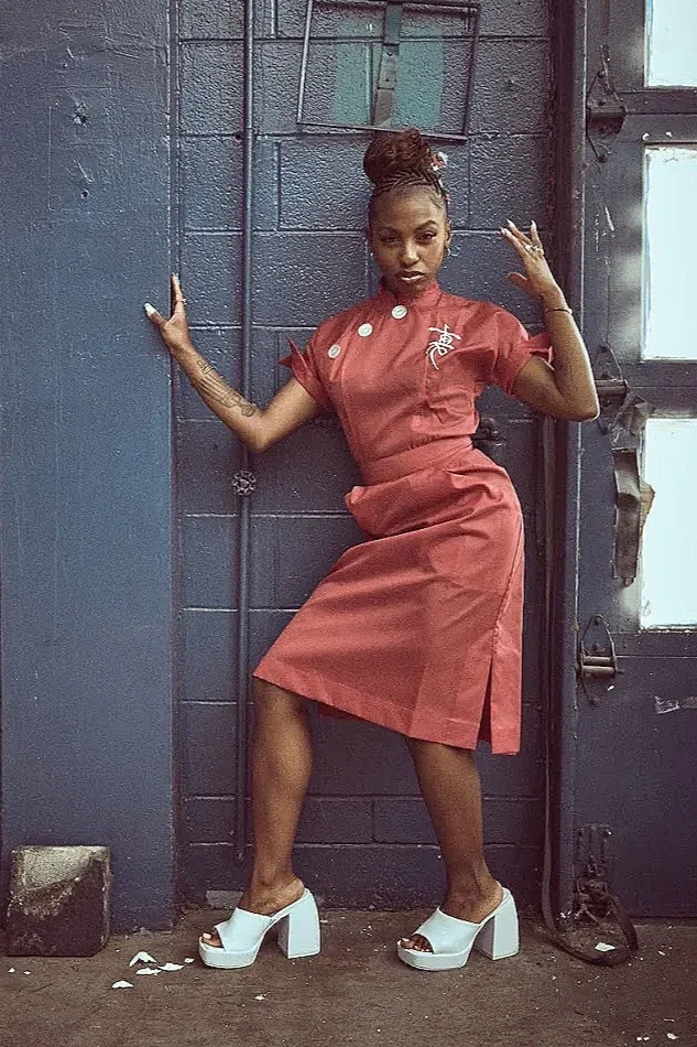 Woman wearing a vintage red dress posed against an industrial wall, showcasing curated dresses from the Fashion to the People Premium Vintage collection.
