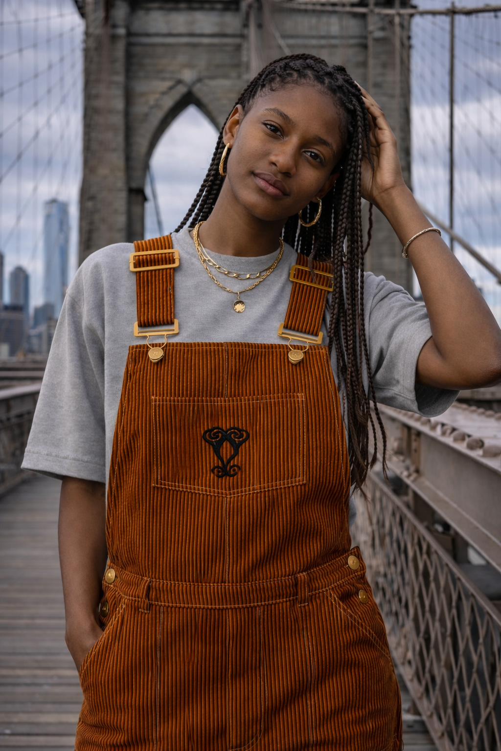 Model wearing rust corduroy overalls from the FTTP circular streetwear collection on the Brooklyn Bridge.