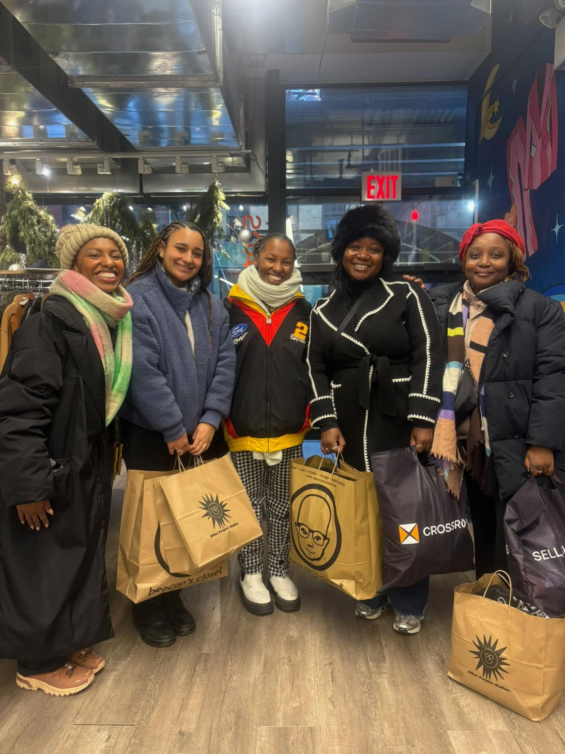 Group of women smiling with vintage shopping bags inside a thrift store during a Fashion to the People guided vintage shopping tour.