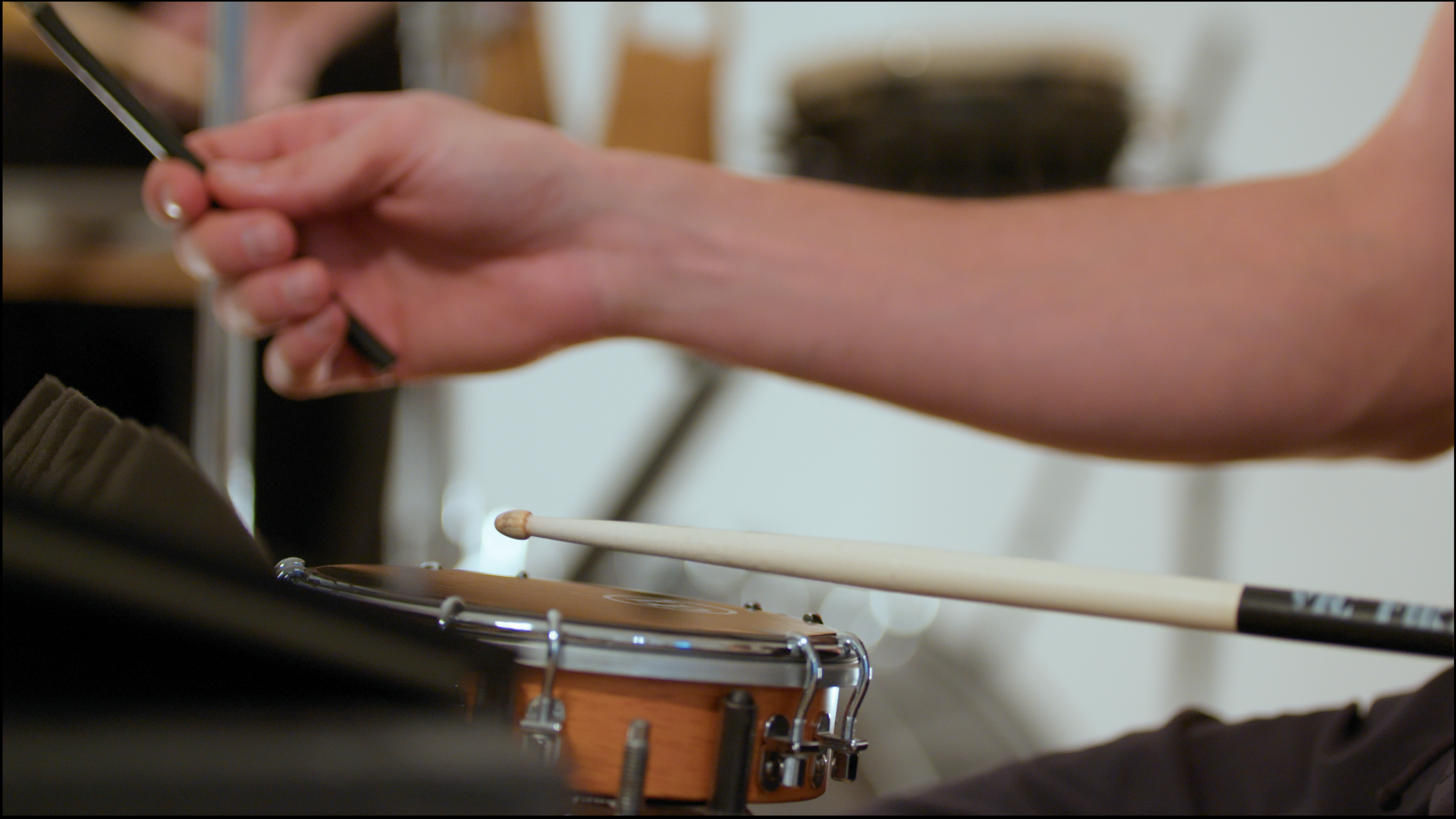 5. A close-up image of a percussionist playing a mounted tamborim with a drum stick.