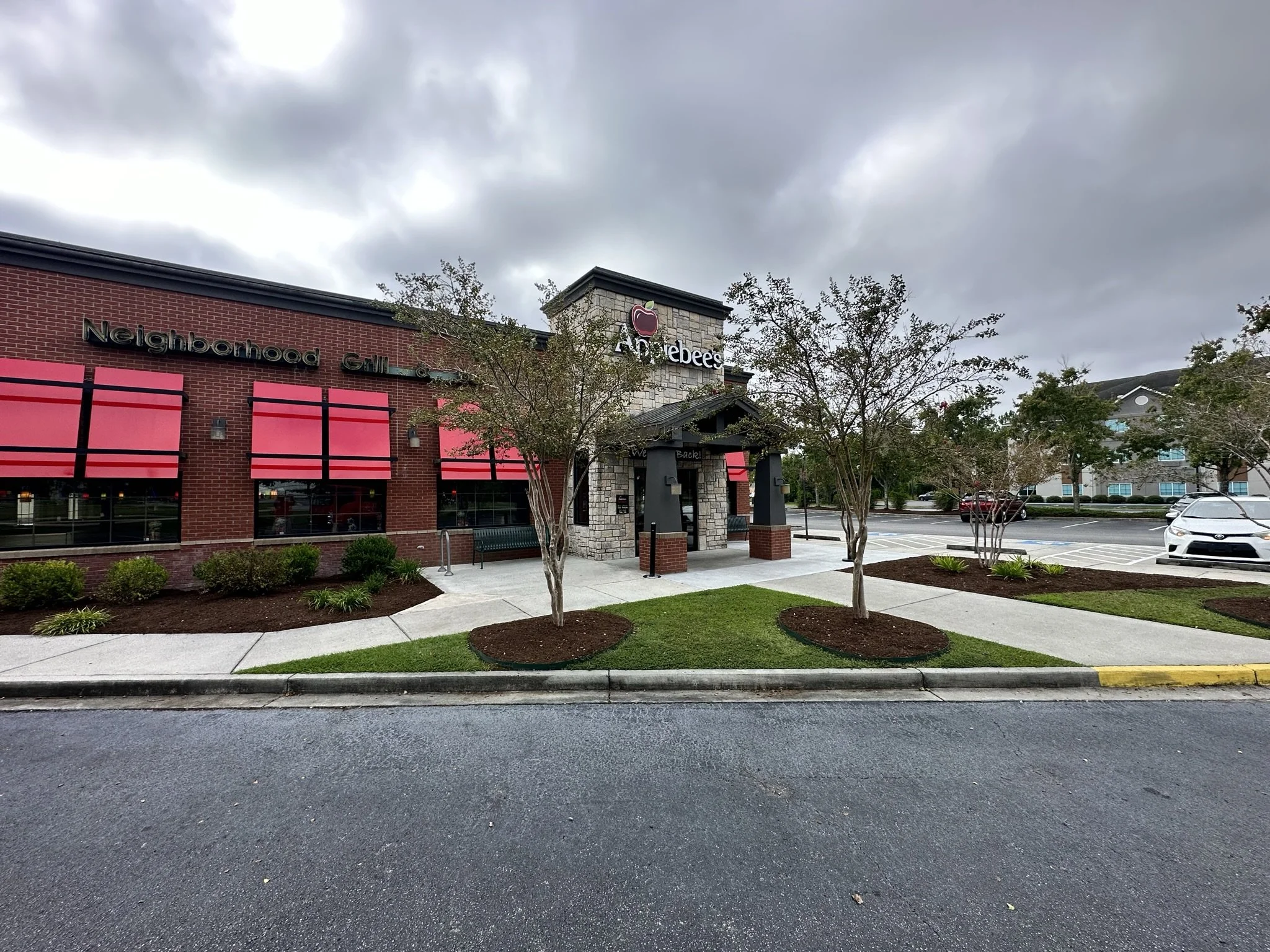 Exterior view of a Restaurant called Applebee's with trees, sidewalk, parking lot, and cloudy sky