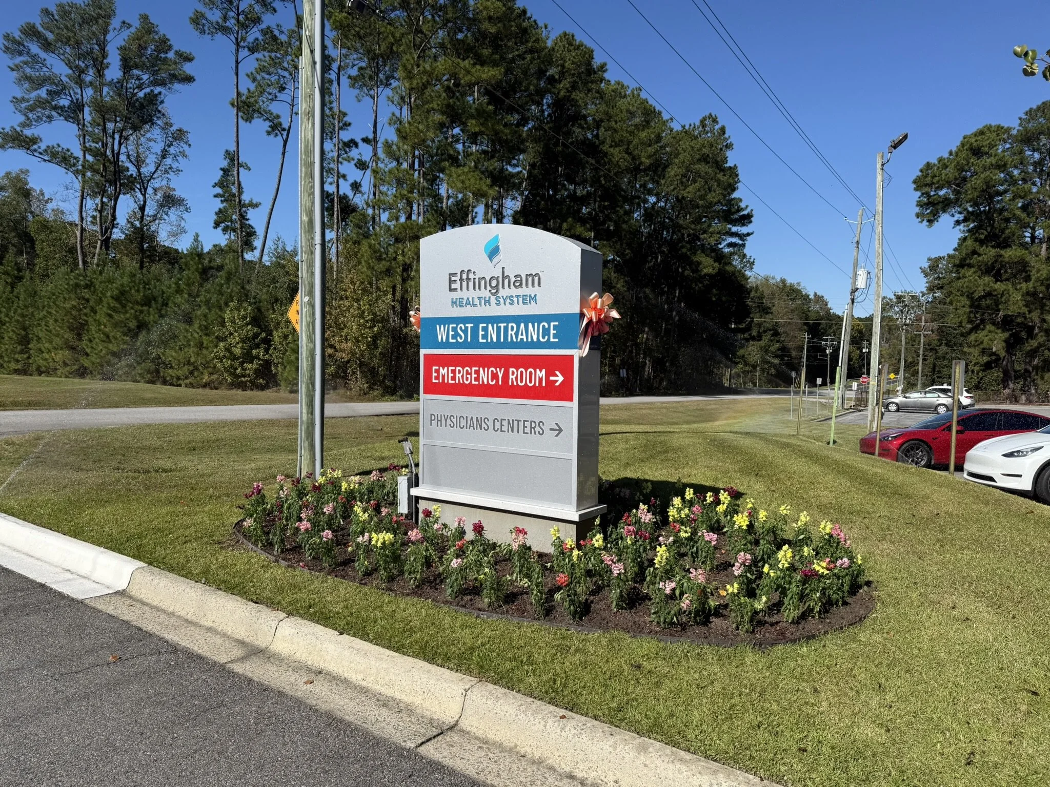 Signboard for Effingham Health System showing directions to West Entrance, Emergency Room, and Physicians Centers, with a flower bed in front.