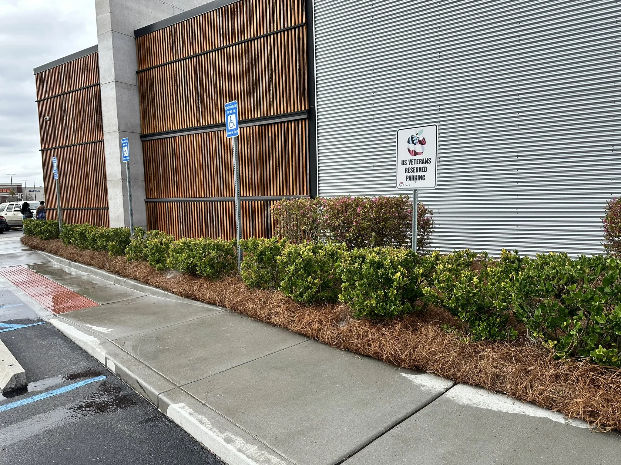Parking lot with handicapped parking signs, a building with wood and metal paneling, and a sign indicating US veterans reserved parking.