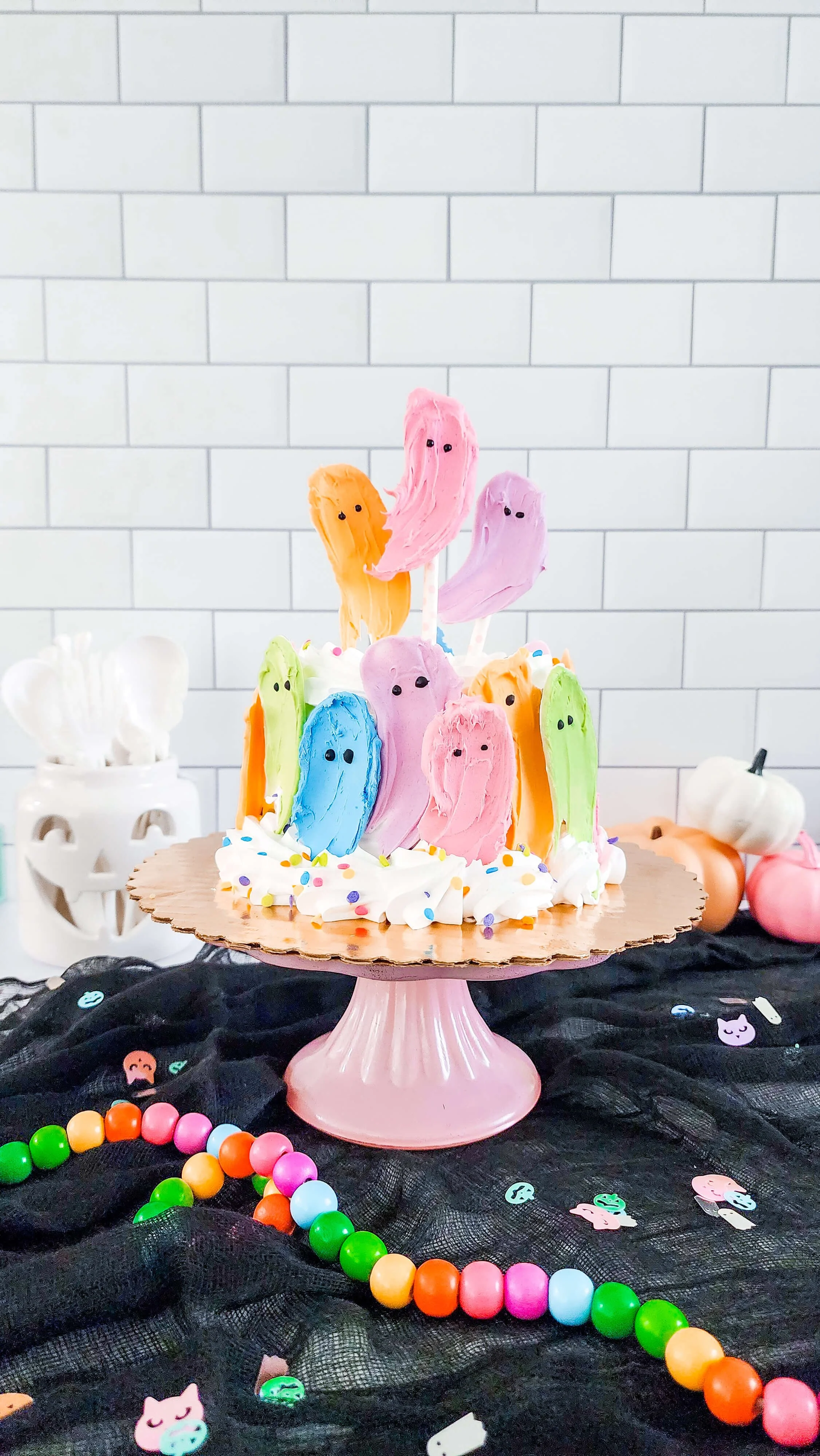 White cake on cake stand with rainbow colored chocolate ghosts