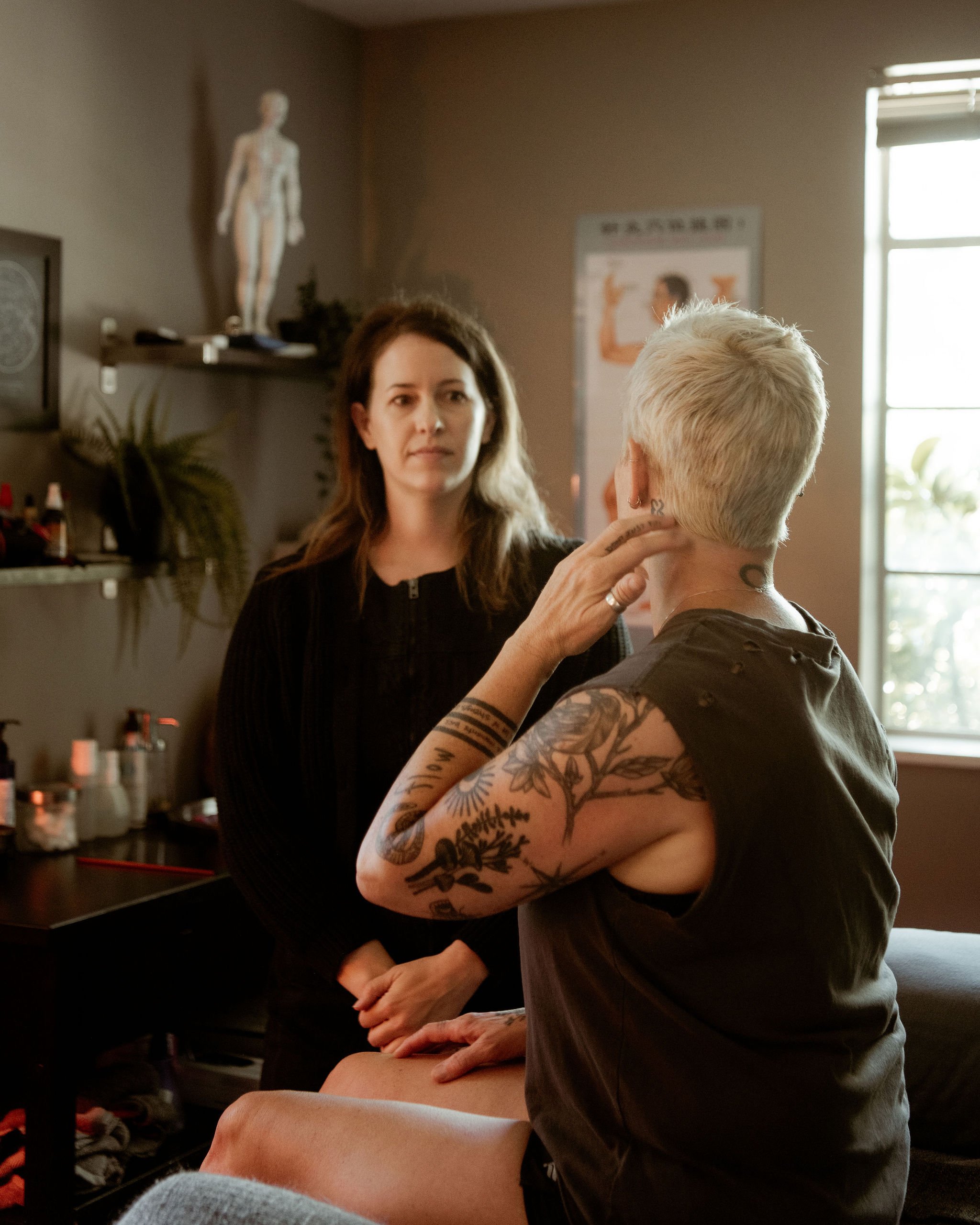 A person receiving a tattoo on their back from an artist. The tattoo features a detailed design, possibly of a bird or dragon.