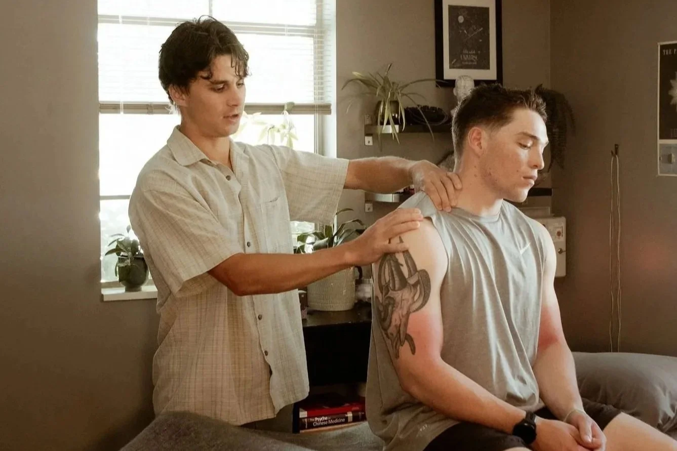 A person receiving a tattoo on their back from an artist. The tattoo features a detailed design, possibly of a bird or dragon.