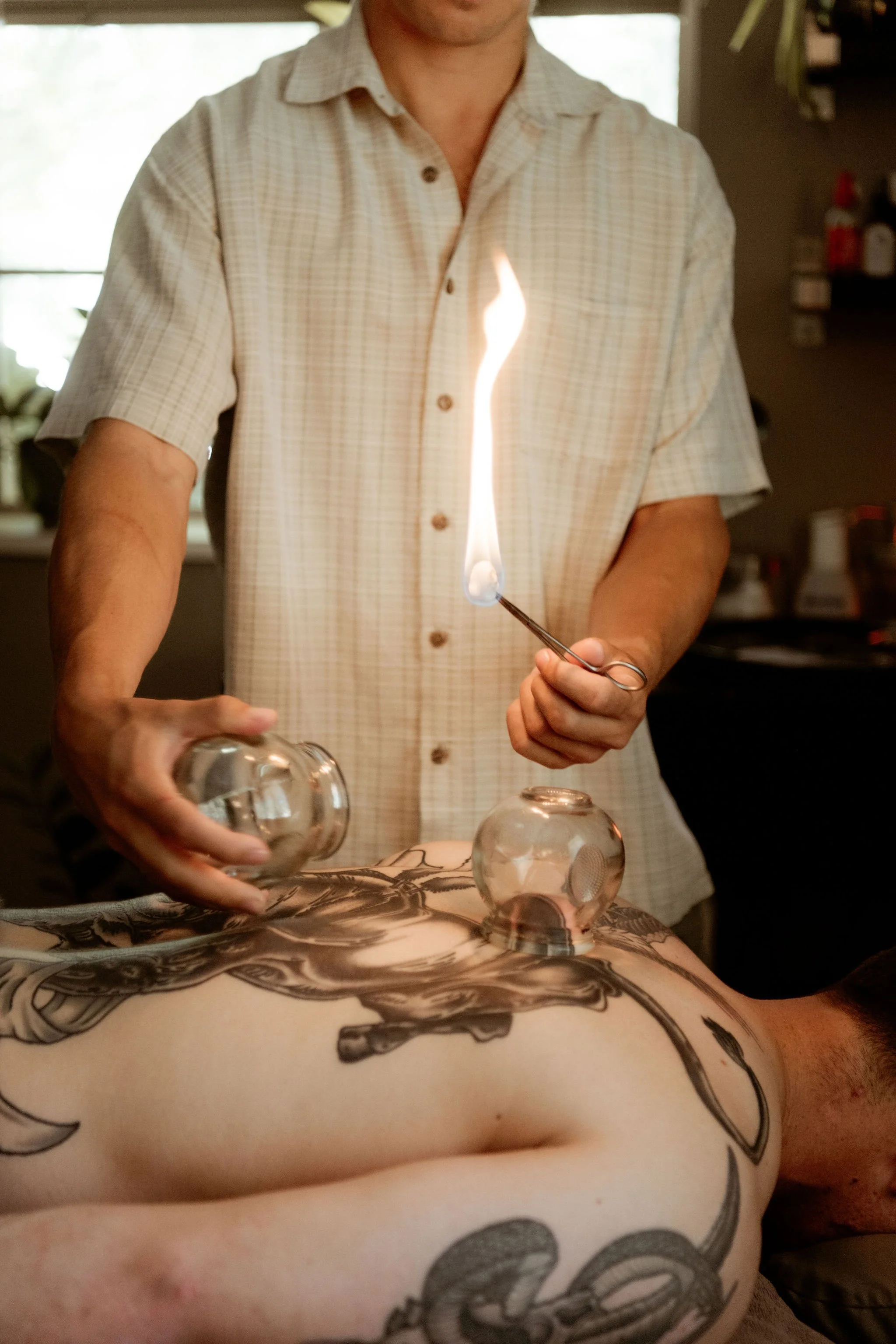 A person receiving a tattoo on their back from an artist. The tattoo features a detailed design, possibly of a bird or dragon.