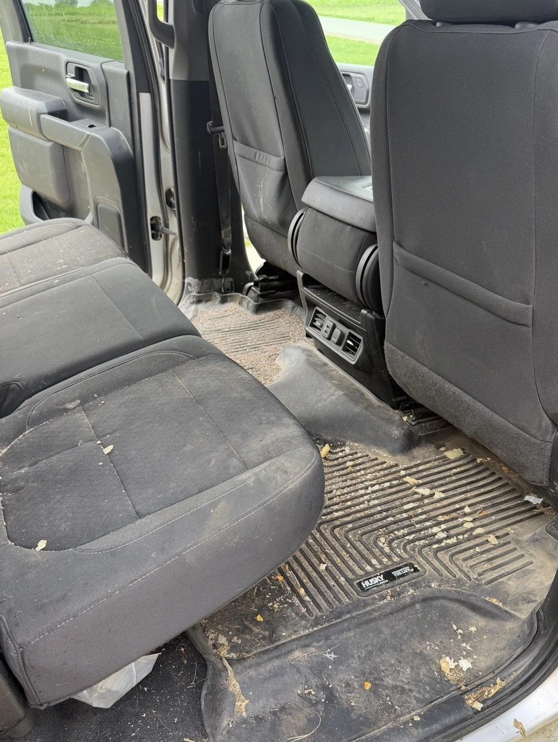 The back seat area of a dirty, used vehicle with muddy floor mats and dust on the seats.