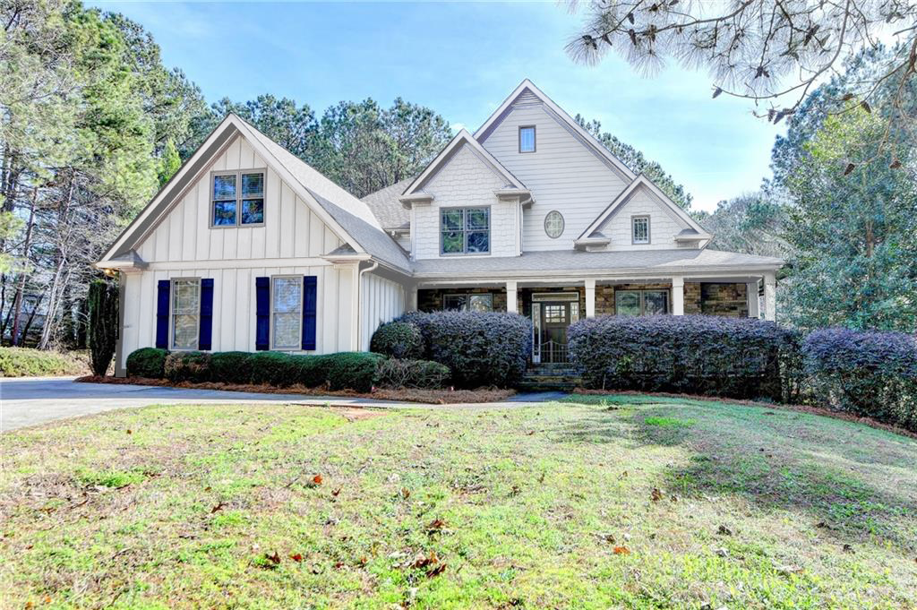 Front view of a large suburban house with gabled roof, white siding, and blue window shutters, surrounded by manicured bushes and trees.