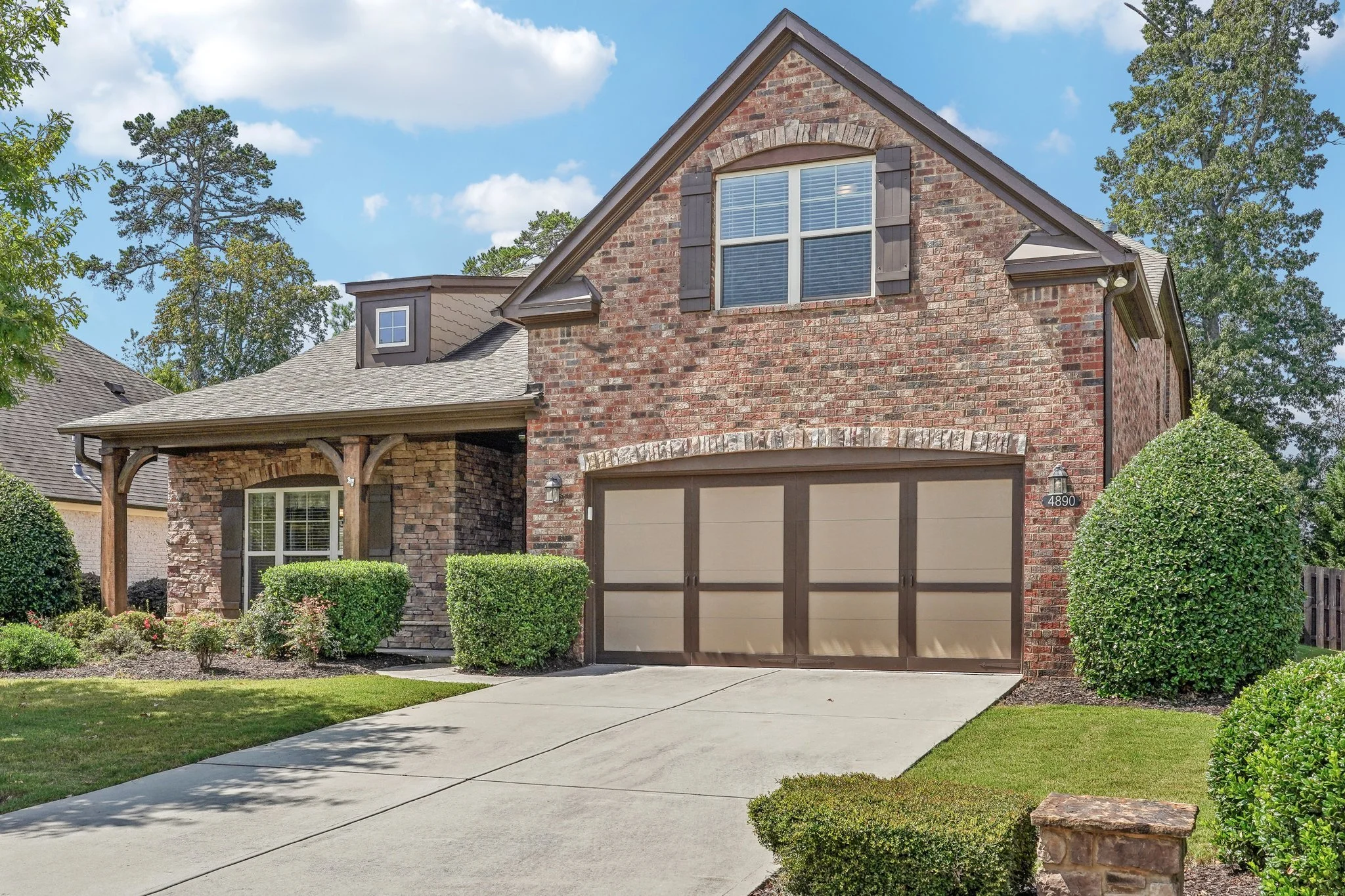 Brick house with garage, front lawn, and shrubs, under a blue sky