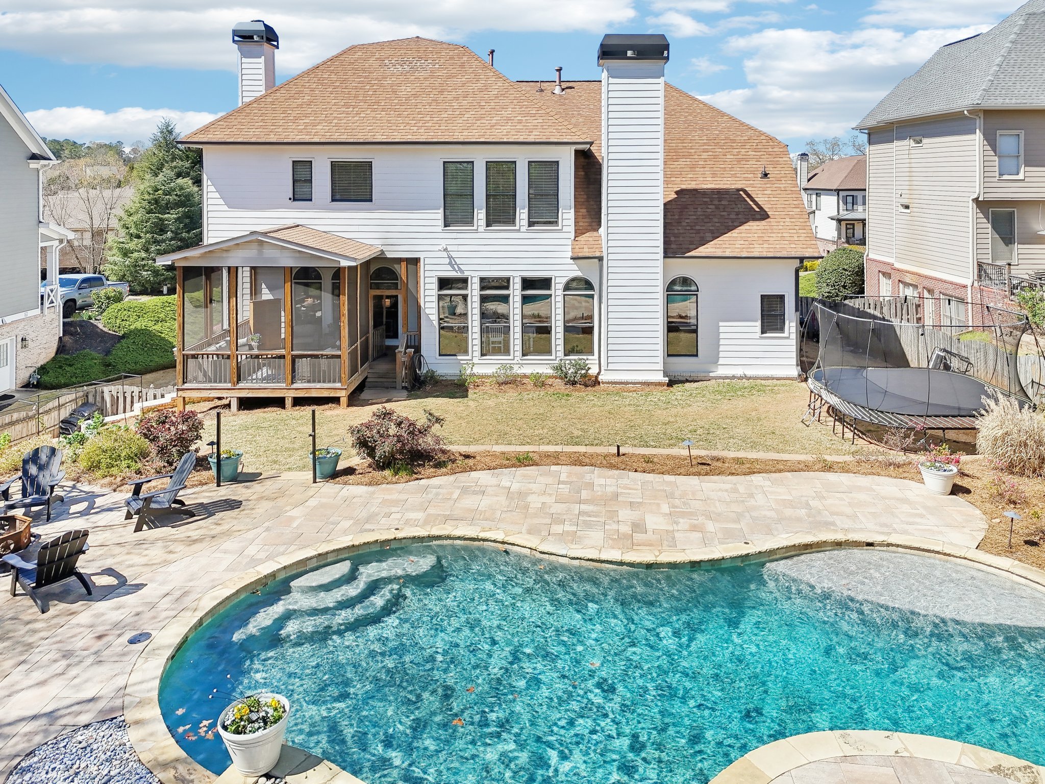 Backyard view of a suburban house with a swimming pool, deck chairs, a trampoline, and a screened porch.