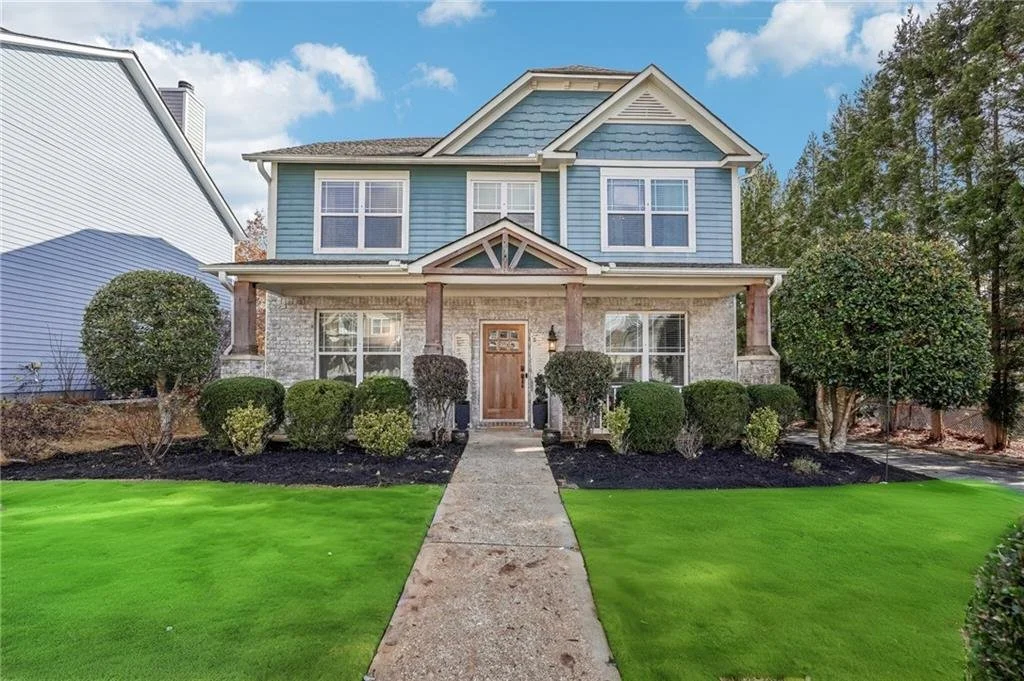 Two-story home with blue siding and white trim, surrounded by green lawn and shrubs, under a clear blue sky.
