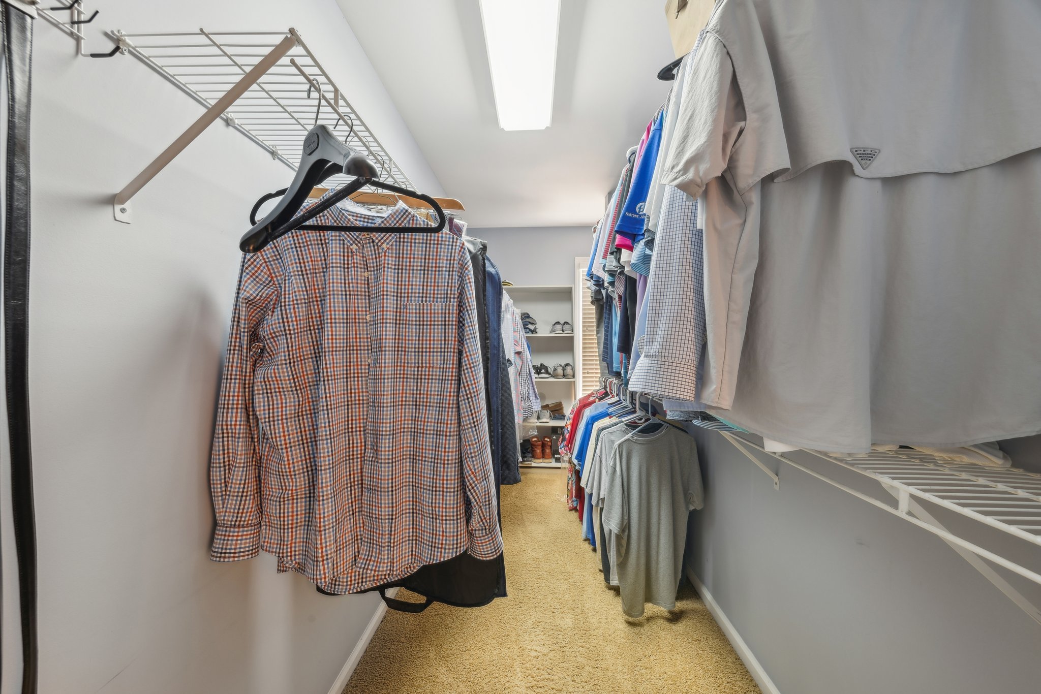 Walk-in closet with clothes hanging on both sides, including shirts and T-shirts, and shelves at the back with shoes.